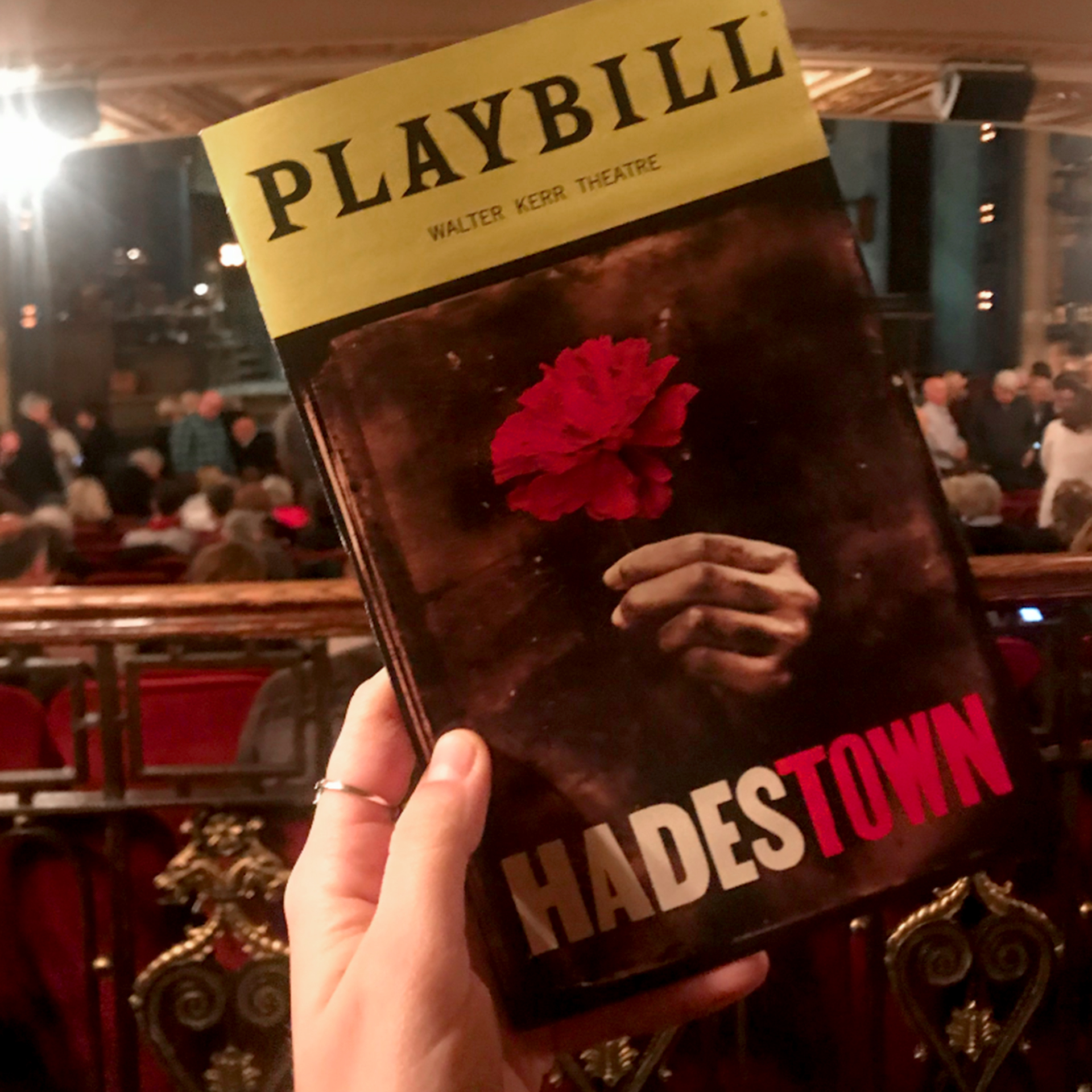 A Playbill booklet for the production of 'Hadestown' is held by a caucasian woman's hand inside of a theater.