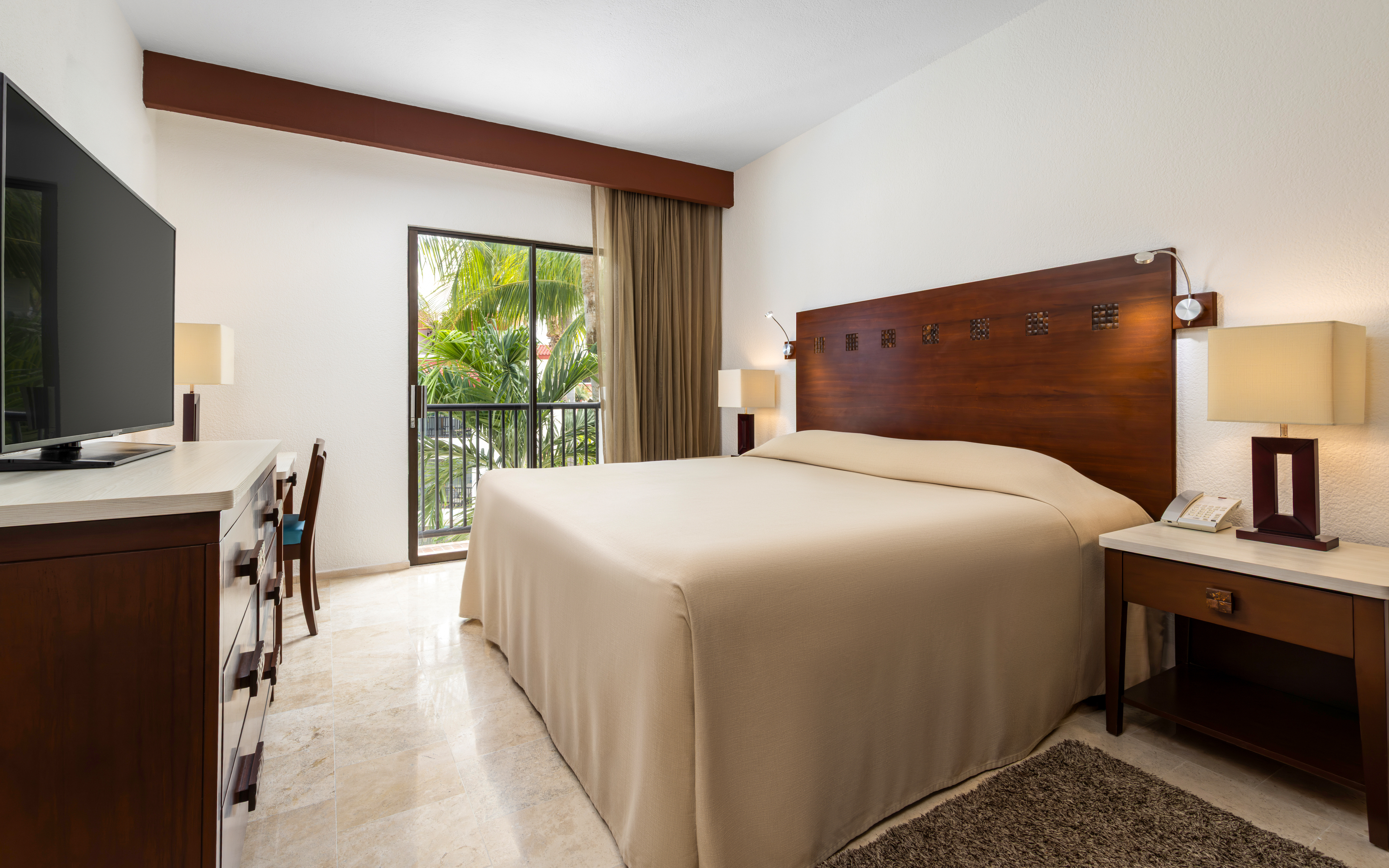 Suite bedroom with king bed and balcony overlooking gardens.