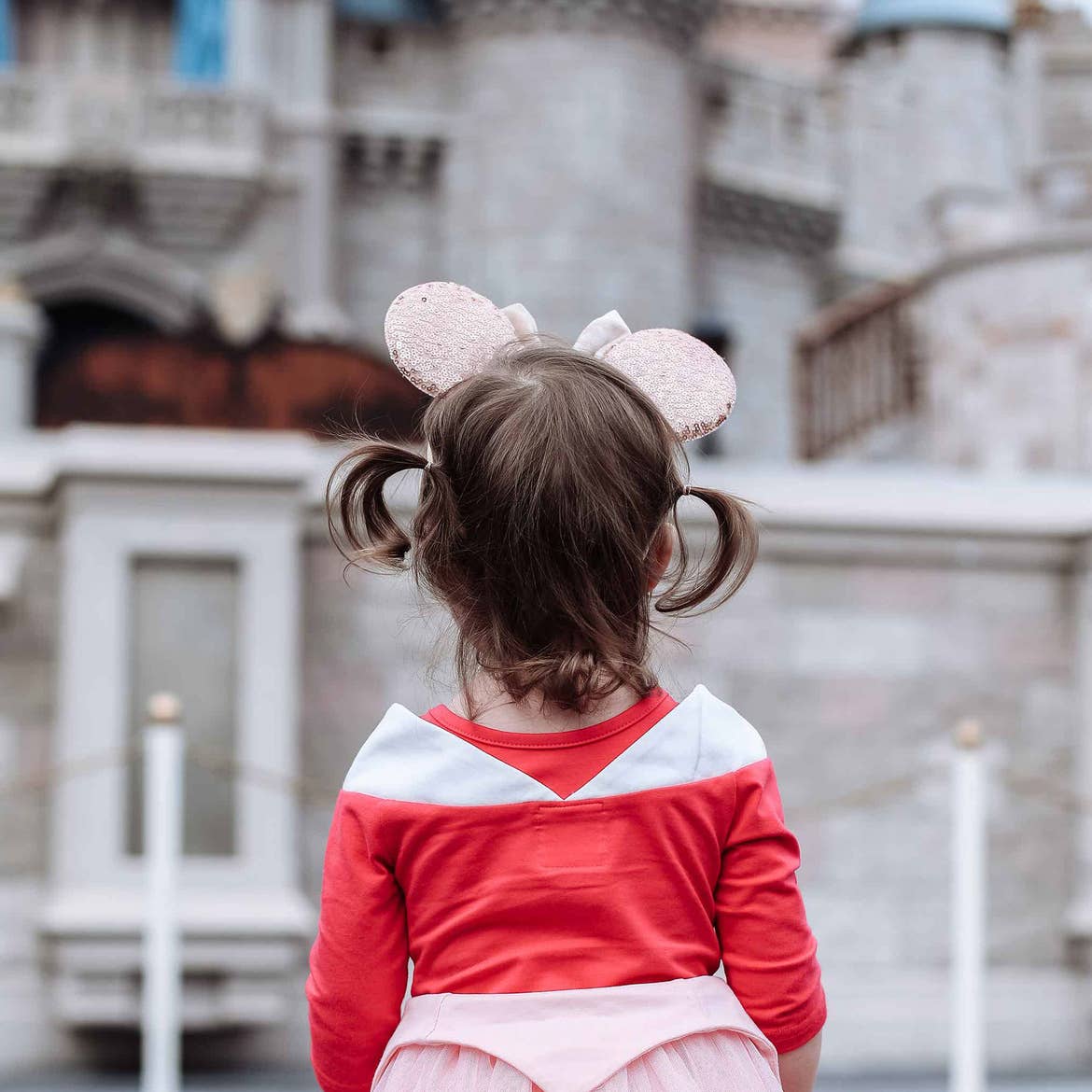 Poppy Bleu stands in front of Cinderella's Castle at Magic Kingdom Park at Walt Disney World® Resort wearing a pink Aurora dress and sparkly Minnie ears.