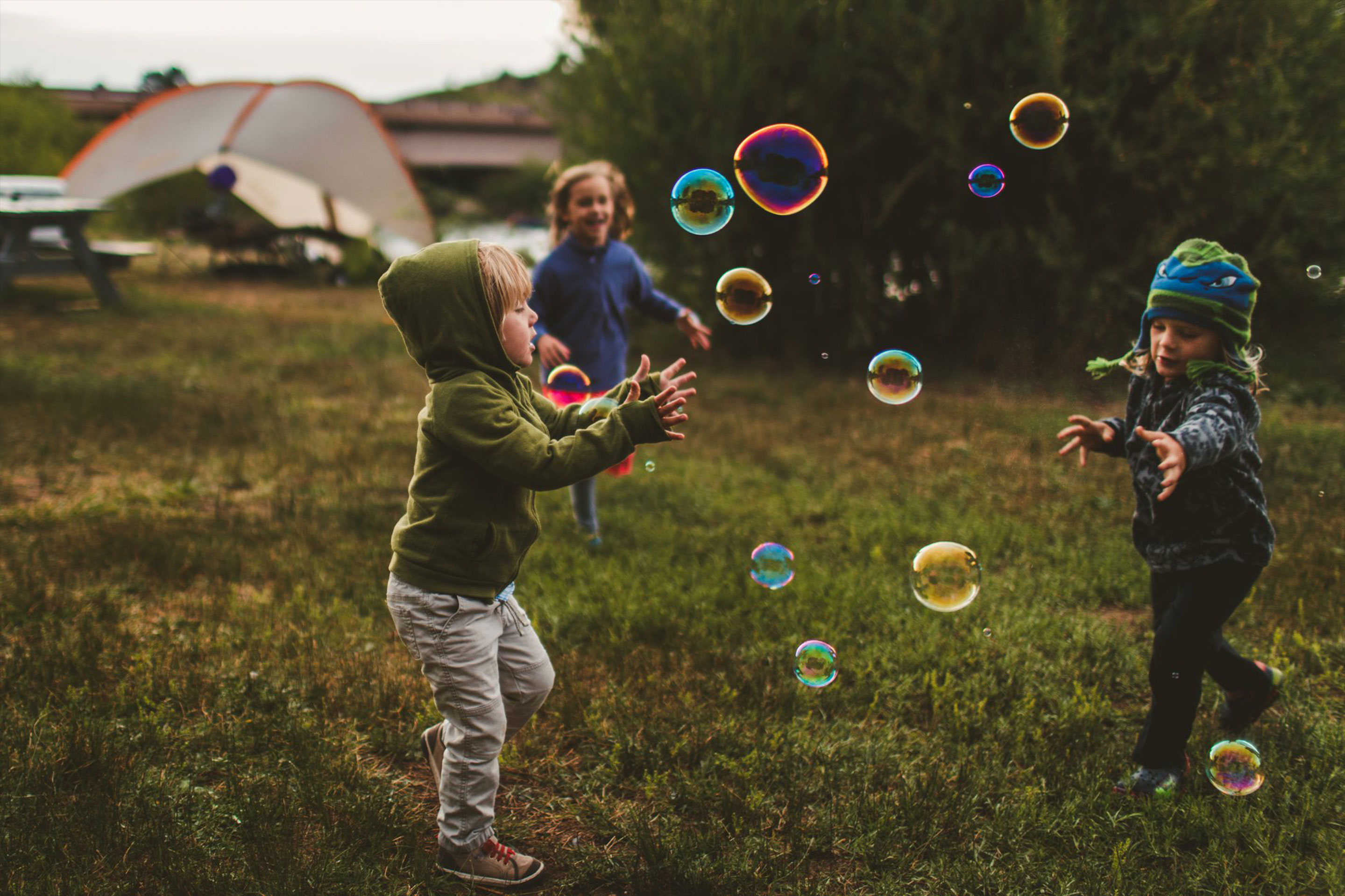 Children pay outdoors whilst chasing bubbles.