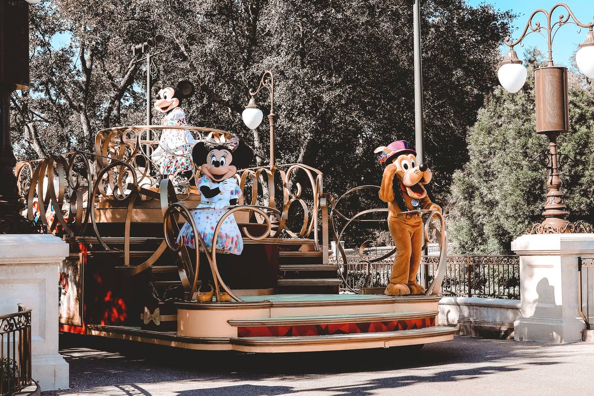 Mickey (back-left), Minnie (front-left) and Pluto (front-right) ride a parade float at Magic Kingdom Park at Walt Disney World® Resort wearing their Birthday Party outfits.