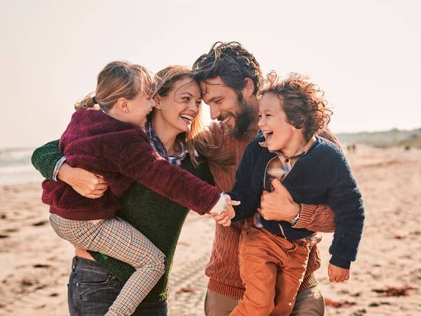 Mom, dad and two kids laughing together at the beach dressed in warm clothing.
