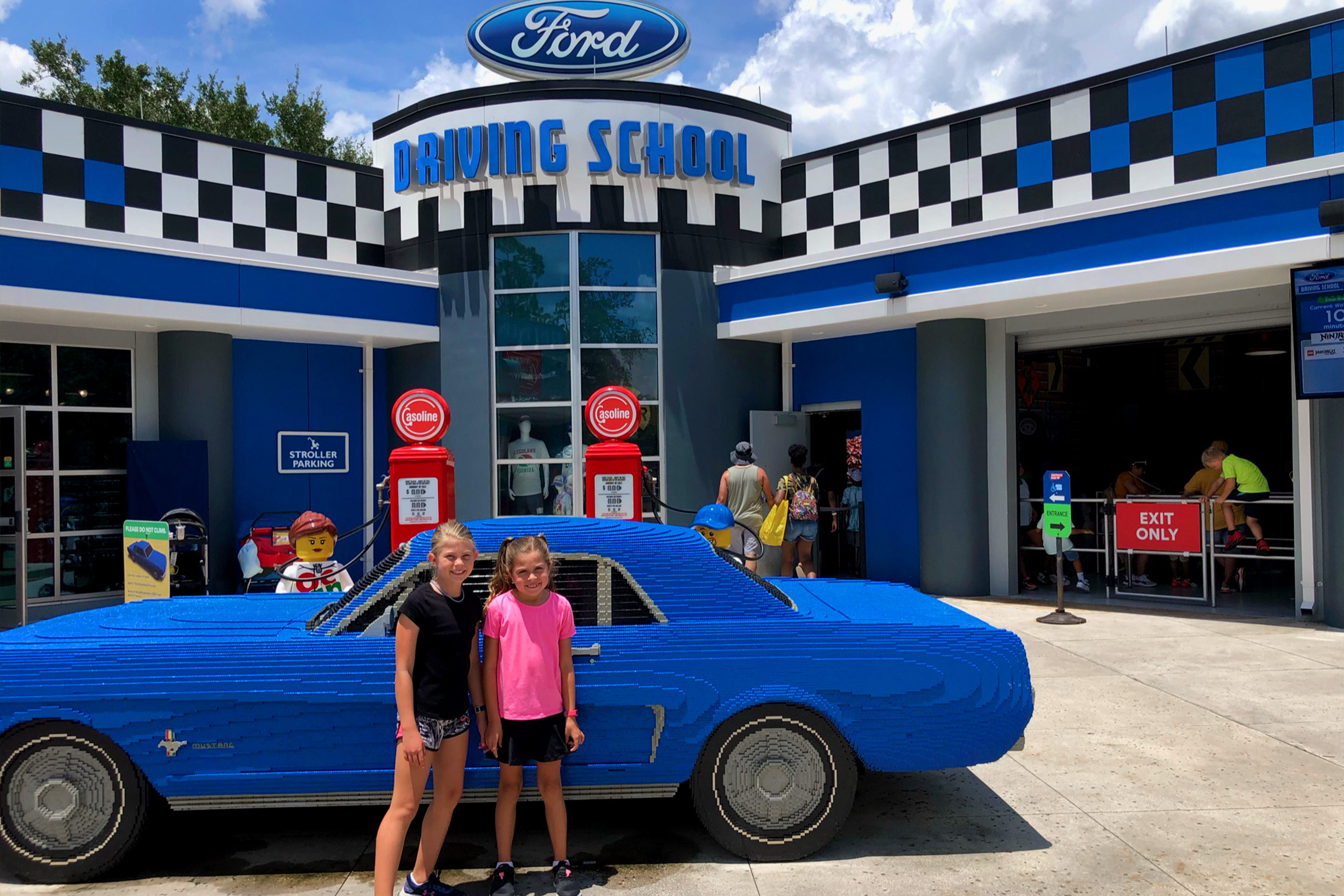 Two young girls stand in front of an auto shop and vintage car made entirely of LEGOS.