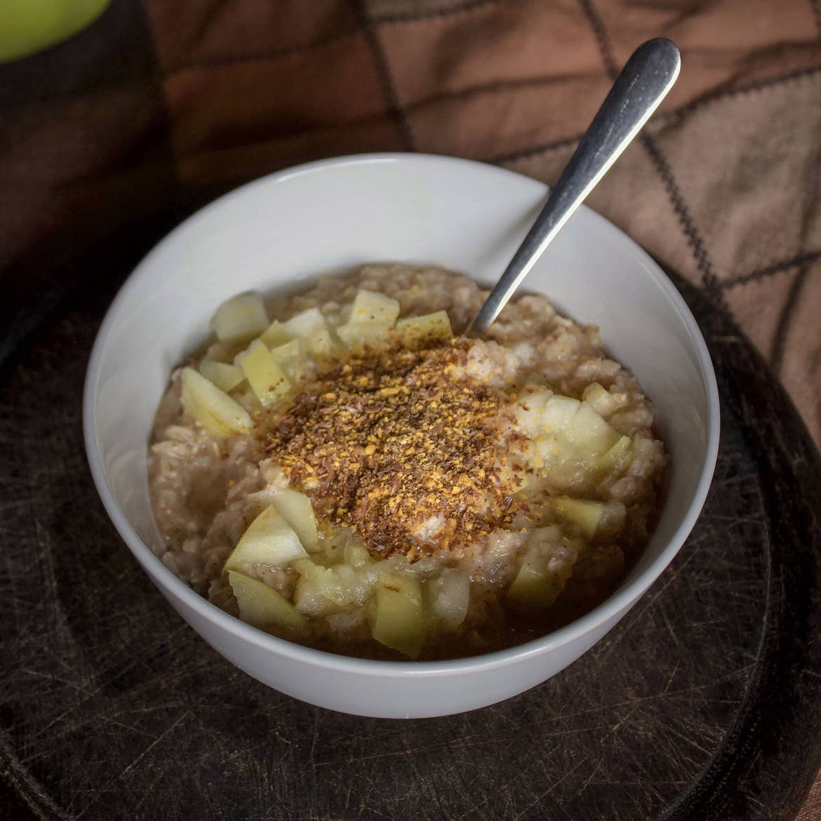 A shot of oatmeal sitting on a table topped with cinnamon, graham cracker crust and apple slices.