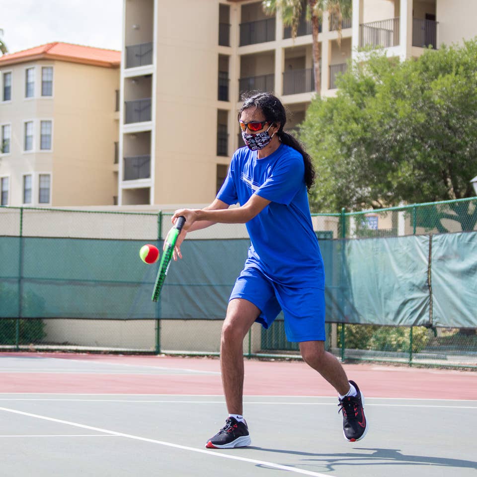 Special Olympic Athlete, Roan Luallen, plays tennis wearing a blue t-shirt and shorts with a safety mask and sunglasses on the courts of our Orange Lake Resort located in Orlando, Florida.