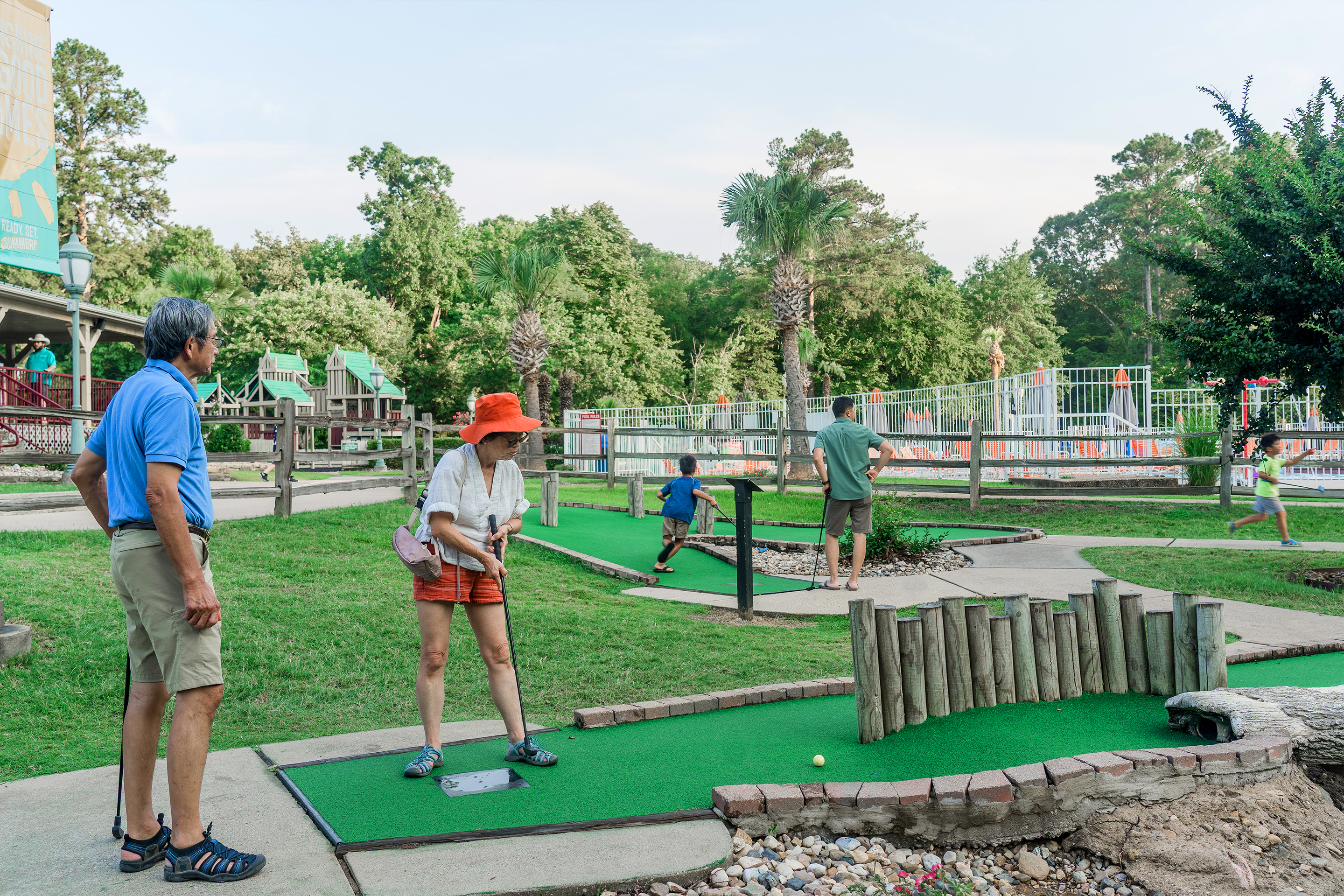 An older Asian man (left) and woman (right) play mini golf near two young Asian boys (right) at our Villages Resort in Flint, Texas.