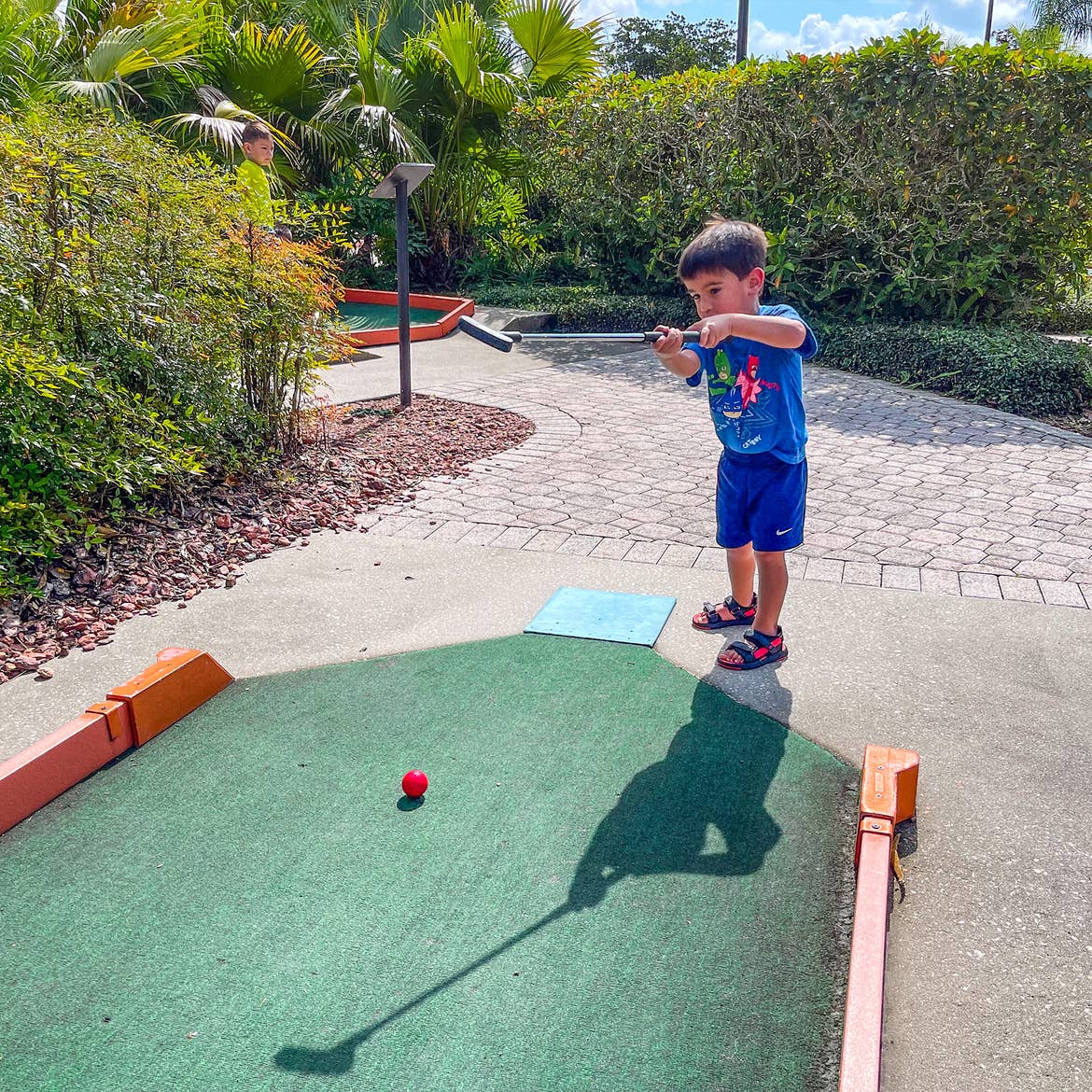 A young boy holds a putter on an outdoor mini golf course.