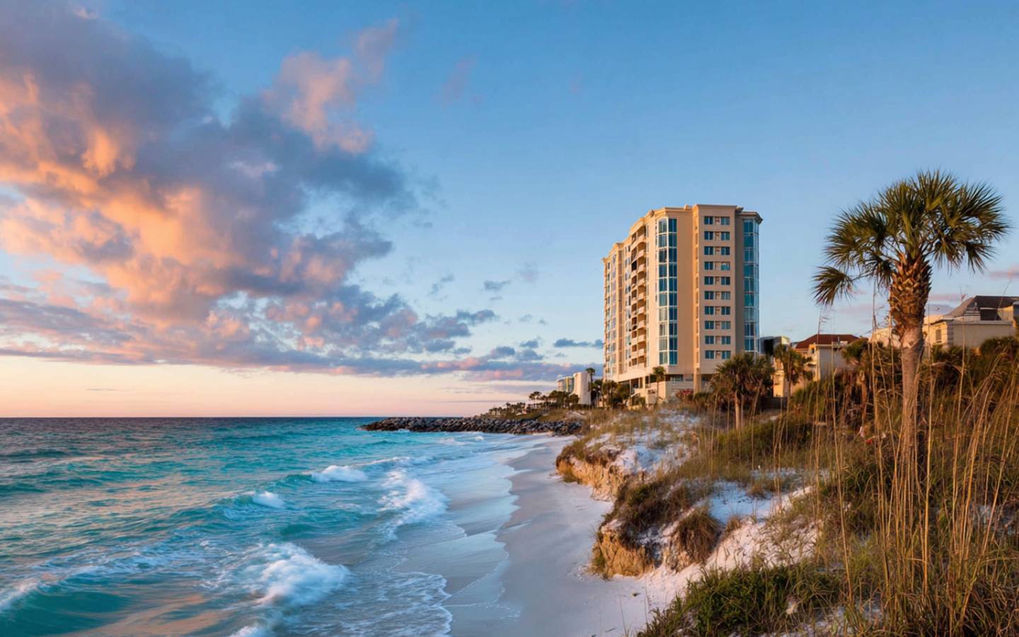 Clouds glowing pink float over rocky shoreline at sunset.