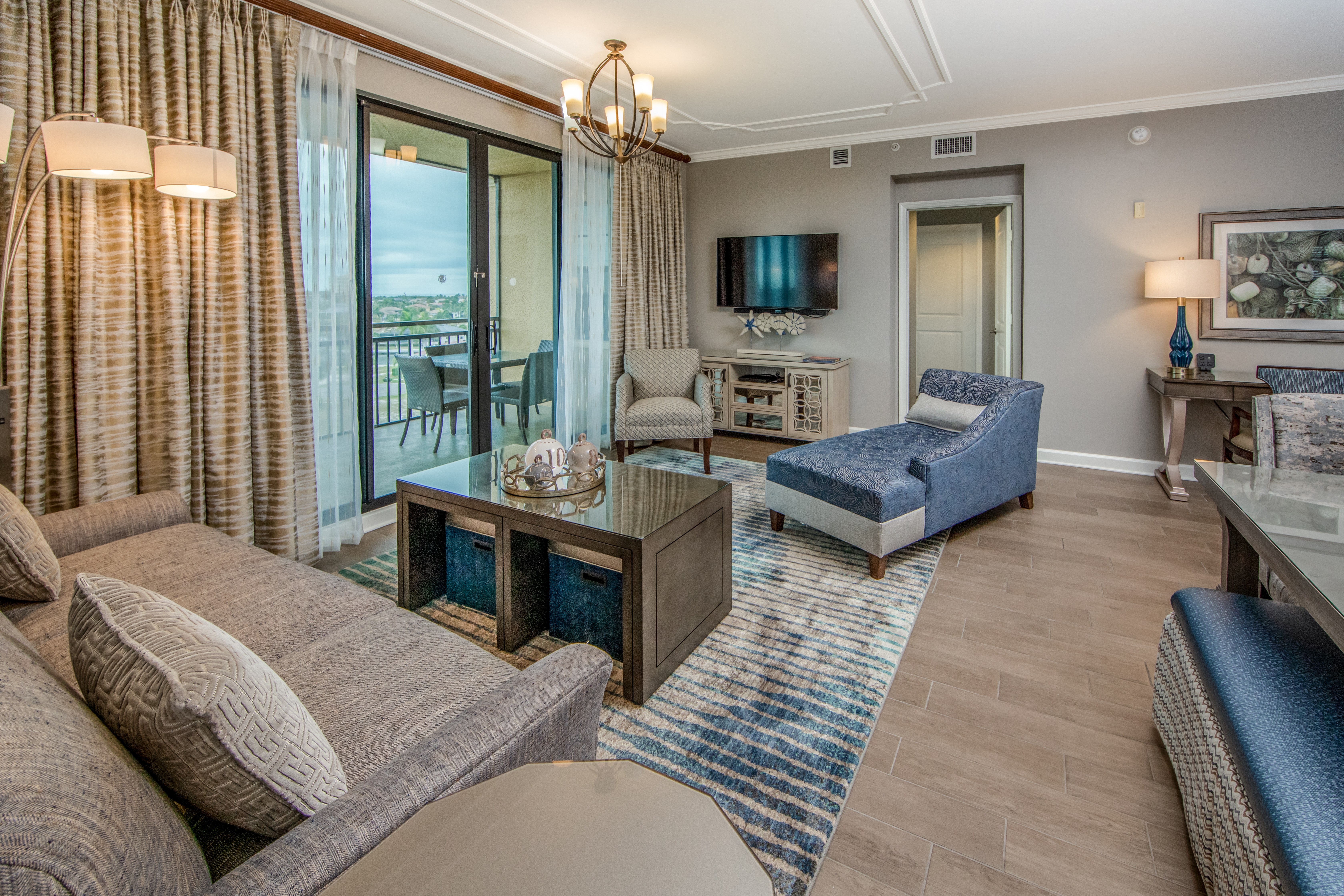 Living room with couch, two accent chairs, a flat screen TV, and access to a furnished balcony in a three-bedroom villa at Sunset Cove Resort in Marco Island, Florida