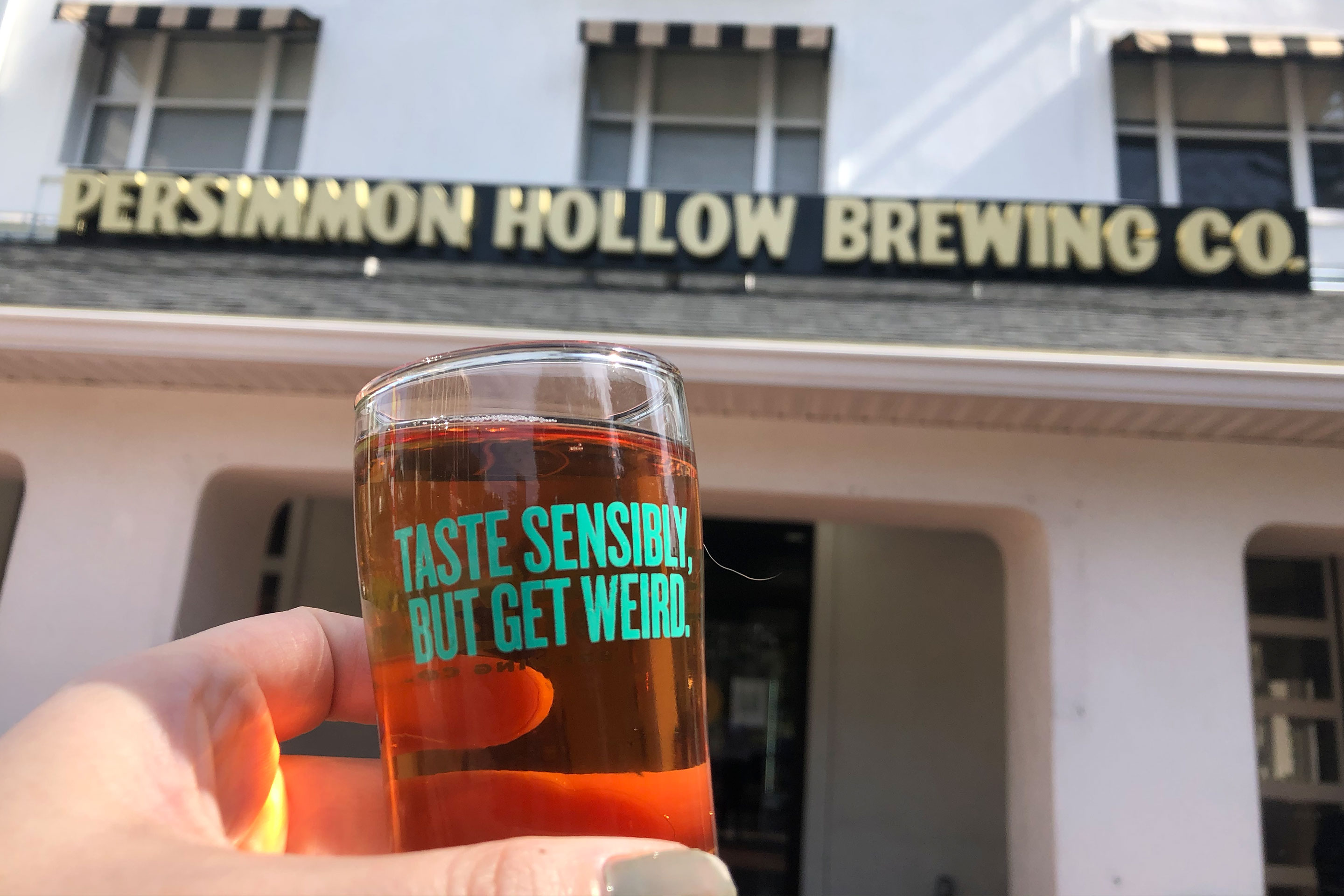 Exterior marquee that reads, 'Persimmon Hollow Brewing Co. and a hand holding a beer glass that reads, 'Taste sensibly, but get weird.'