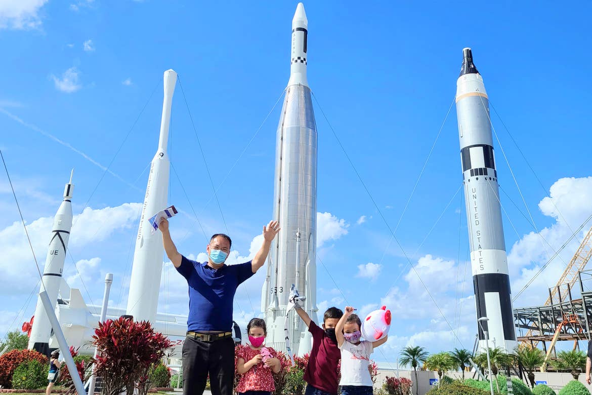 A man and three children pose in front of several decommissioned rockets outdoors under a blue sky.