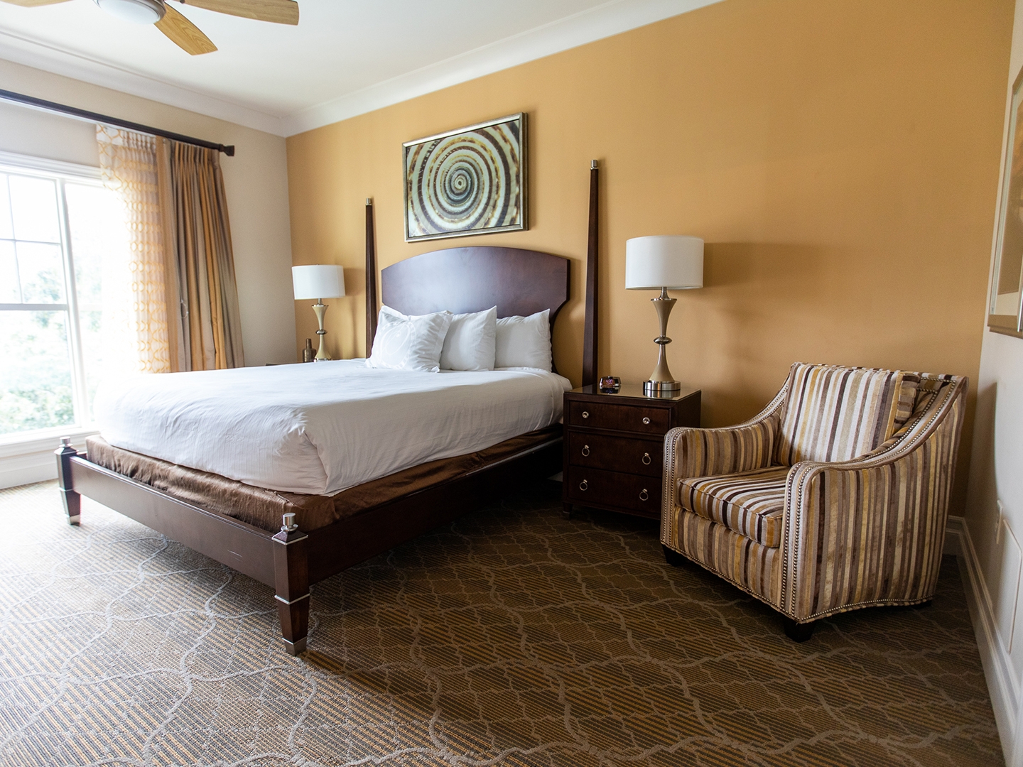Bedroom with a bed, window and chair in a four-bedroom Signature Collection villa at South Beach Resort in Myrtle Beach, South Carolina.