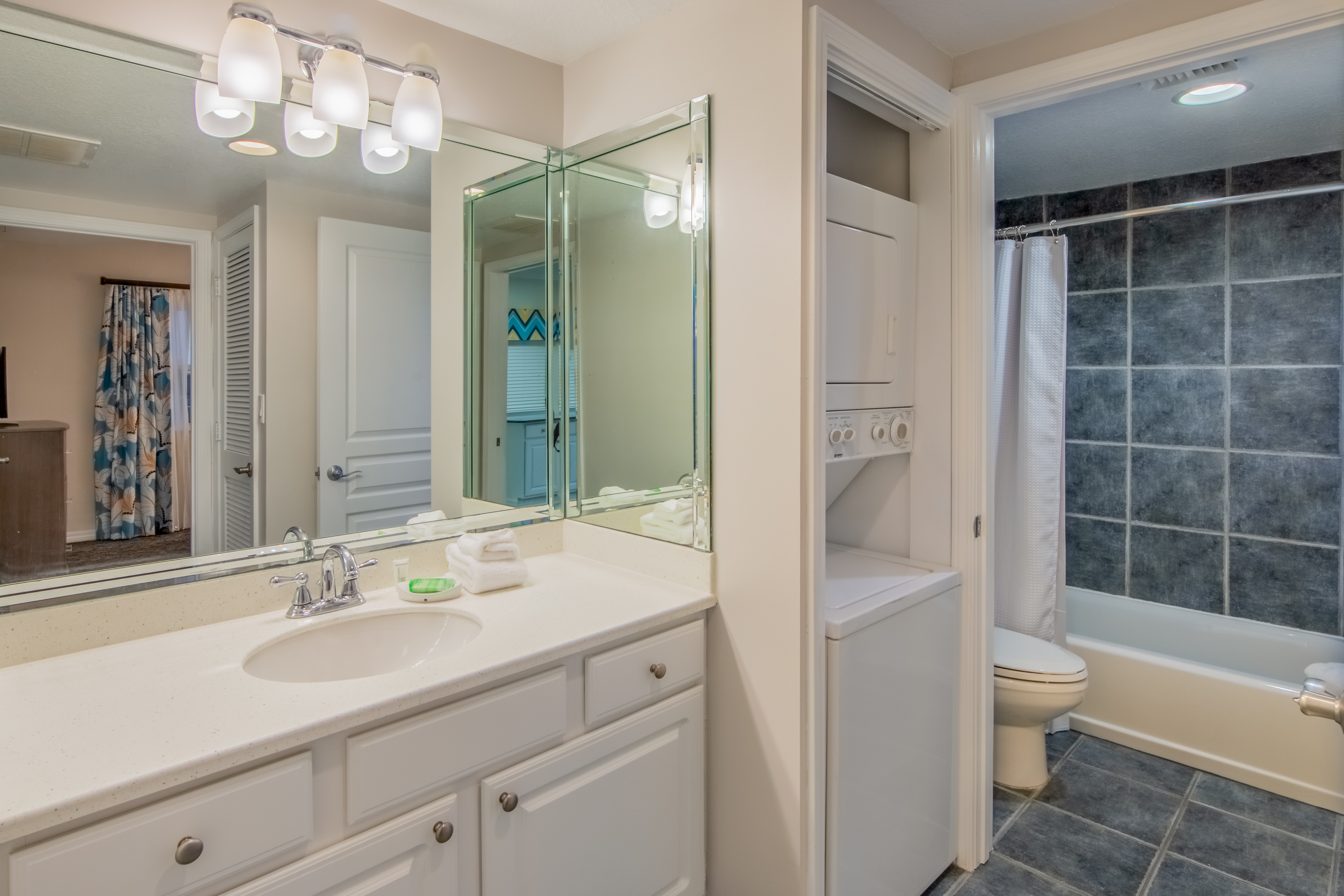 Bathroom with shower/tub combination, toilet, washer/dryer, and sink with large mirror in a two-bedroom villa at Panama City Beach Resort