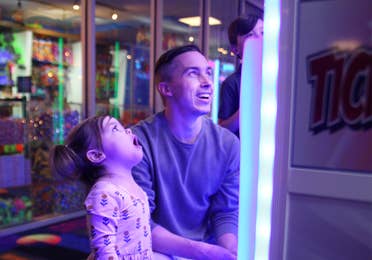 A young man and toddler girl playing video games in a game room.