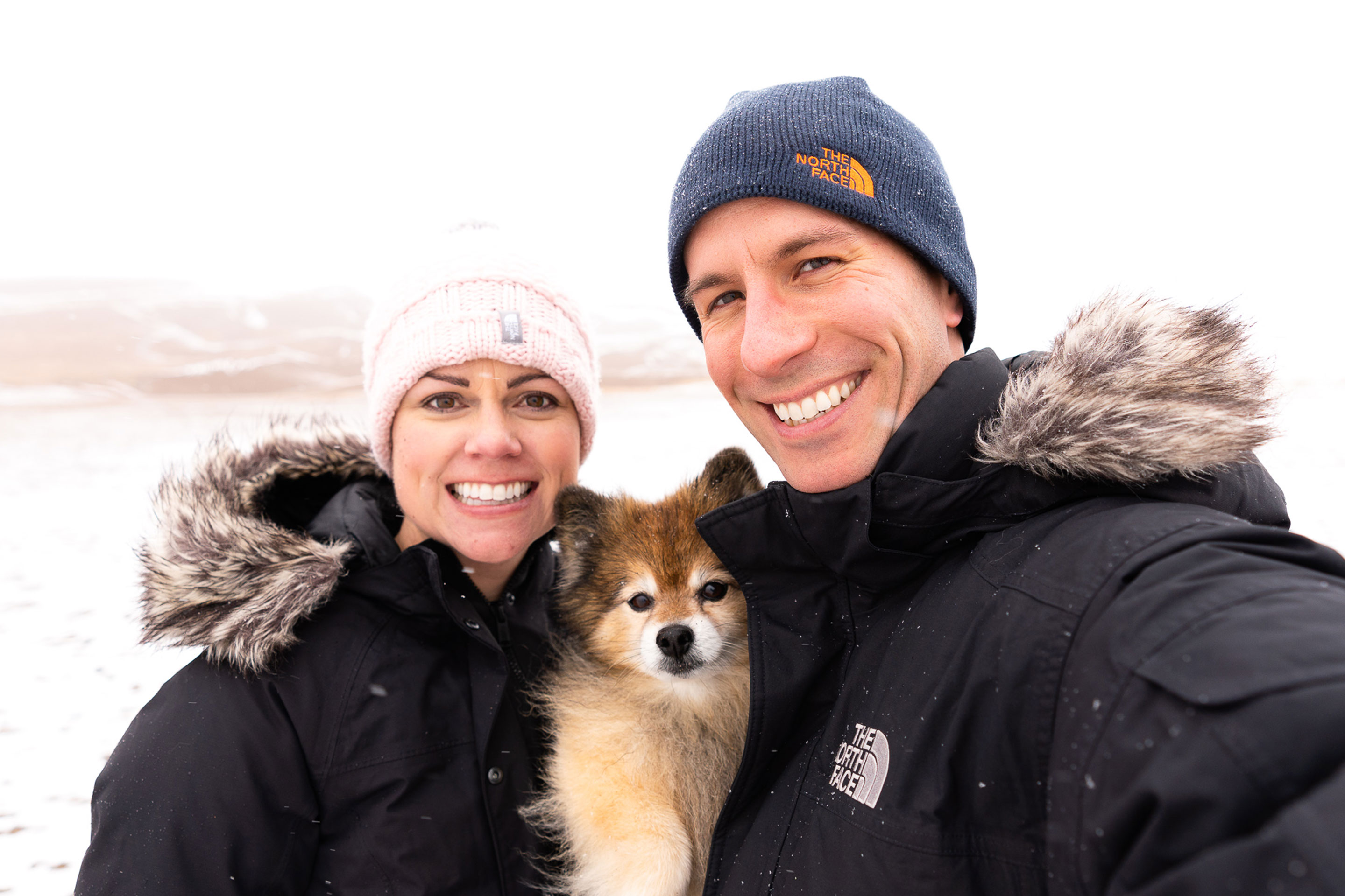 Authors, Lauren Layne and Anthony LeDonne, stand in winter apparel with Bailey the Pomeranian at the Great Sand Dunes National Park and Preserve.