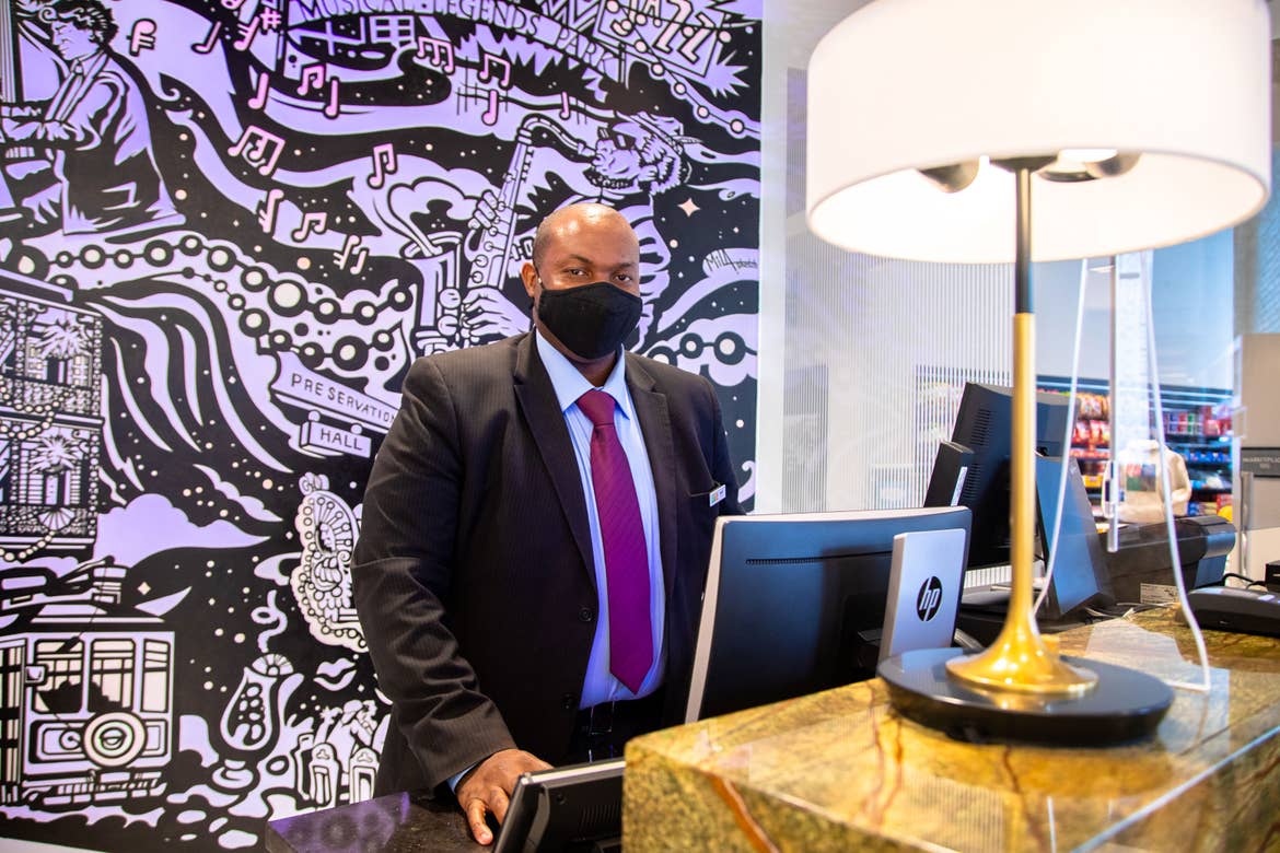 HICV Team Member stands in front of a mural with animated projection mapping in various colors of purple, orange, yellow and magenta featured in the lobby of our resort in New Orleans, Louisiana.