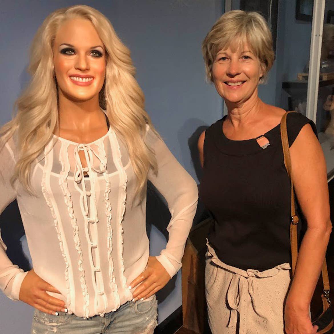 A woman in a black top stands to the right of a wax figure of singer, Carrie Underwood.