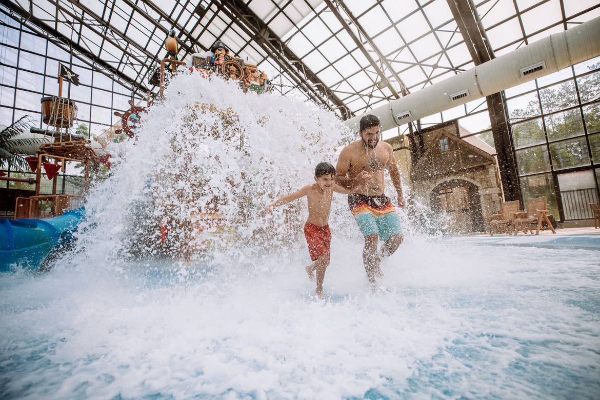 A young boy (left) and a man (right) run from a water park splash pad in an indoor waterpark.