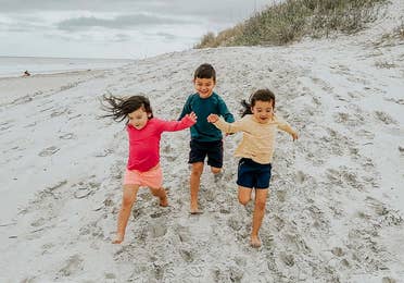 Three toddlers in multi-colored rash guards and board shorts run on a sandy beach.