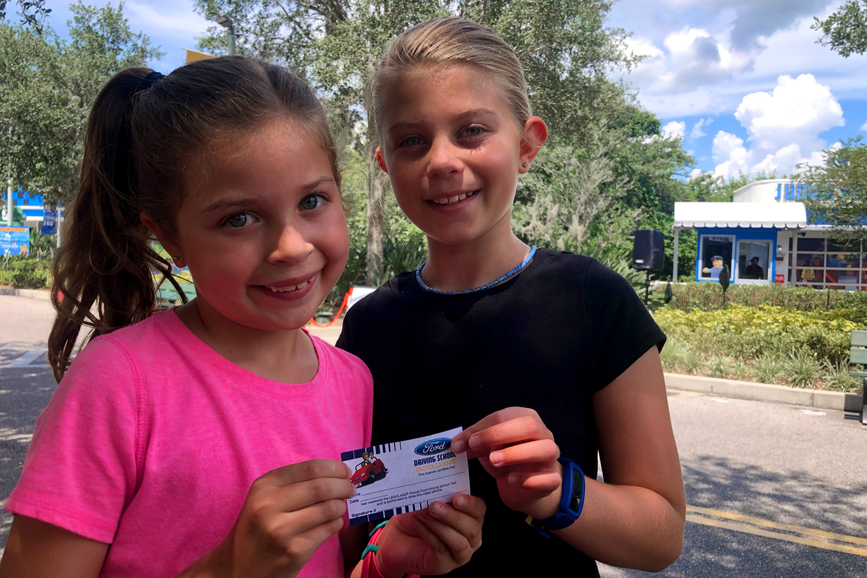 Two young girls stand holding an Unofficial LEGO Drivers License.