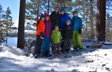 Two adults and five children stand on a snow-covered mountain wearing winter apparel.