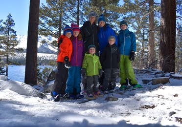 Two adults and five children stand on a snow-covered mountain wearing winter apparel.