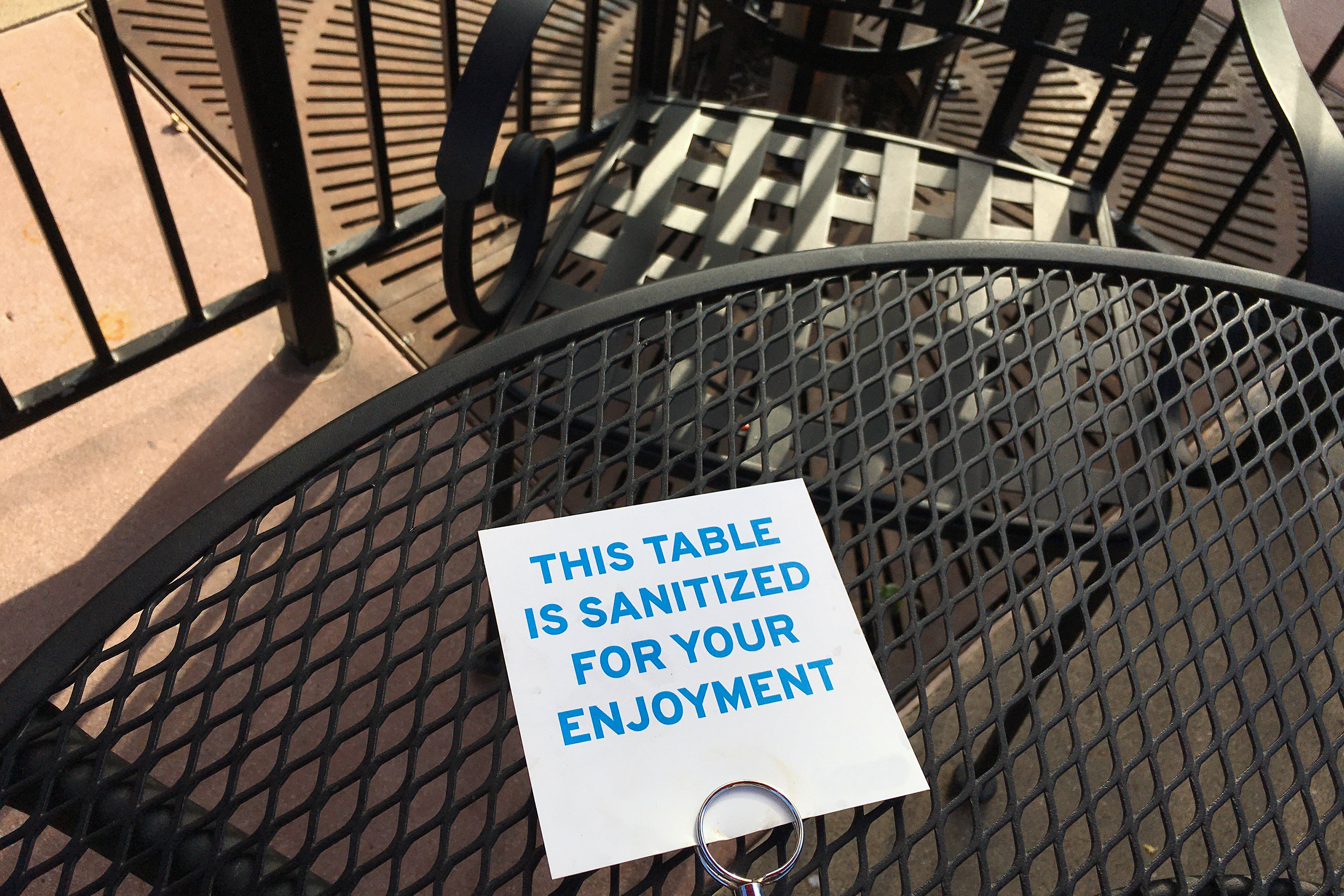 Outdoor black-iron dining table with a sign that reads, 'This table is sanitized for your enjoyment.'