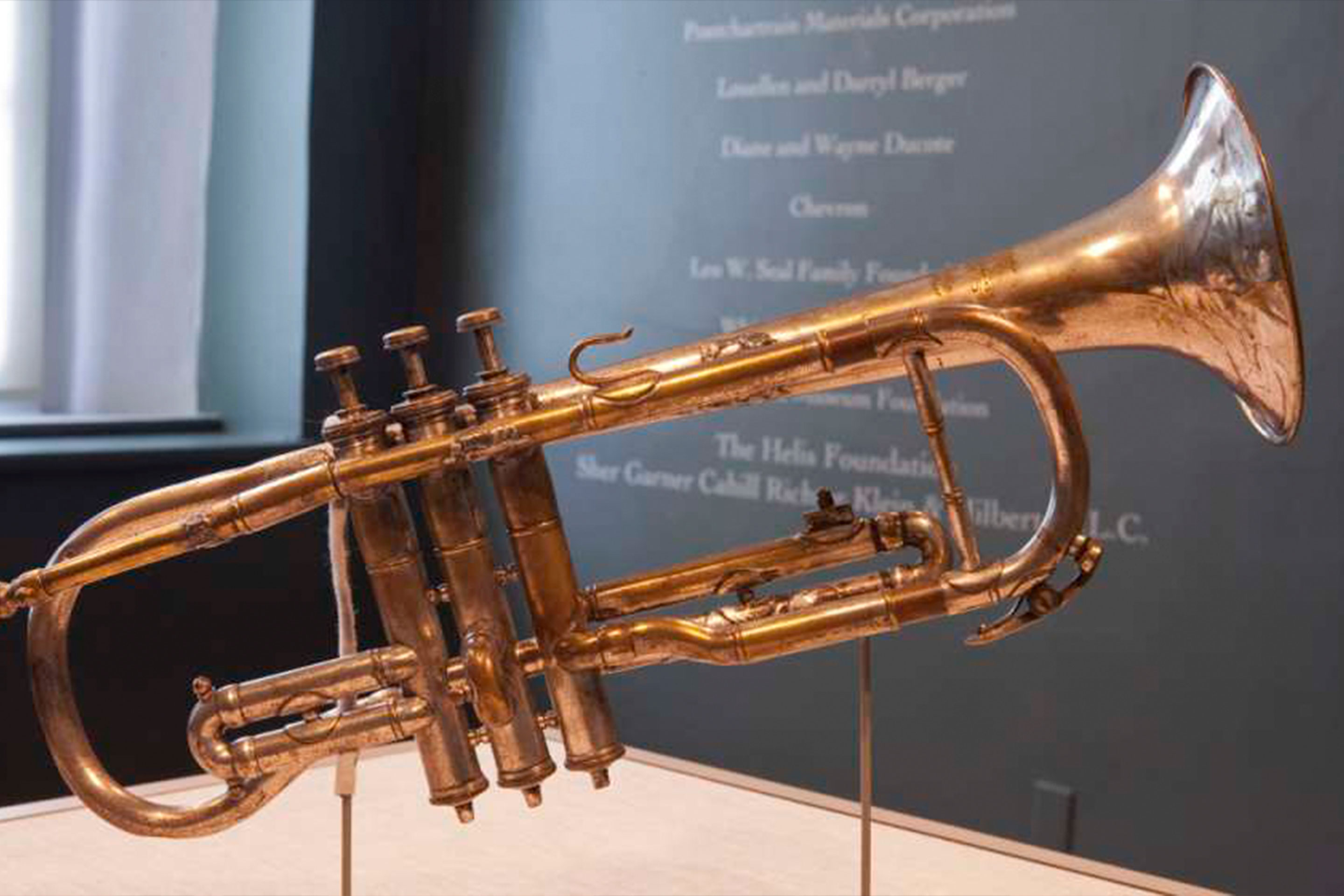 An old trumpet floats above a display near a dark wall with information written on it.