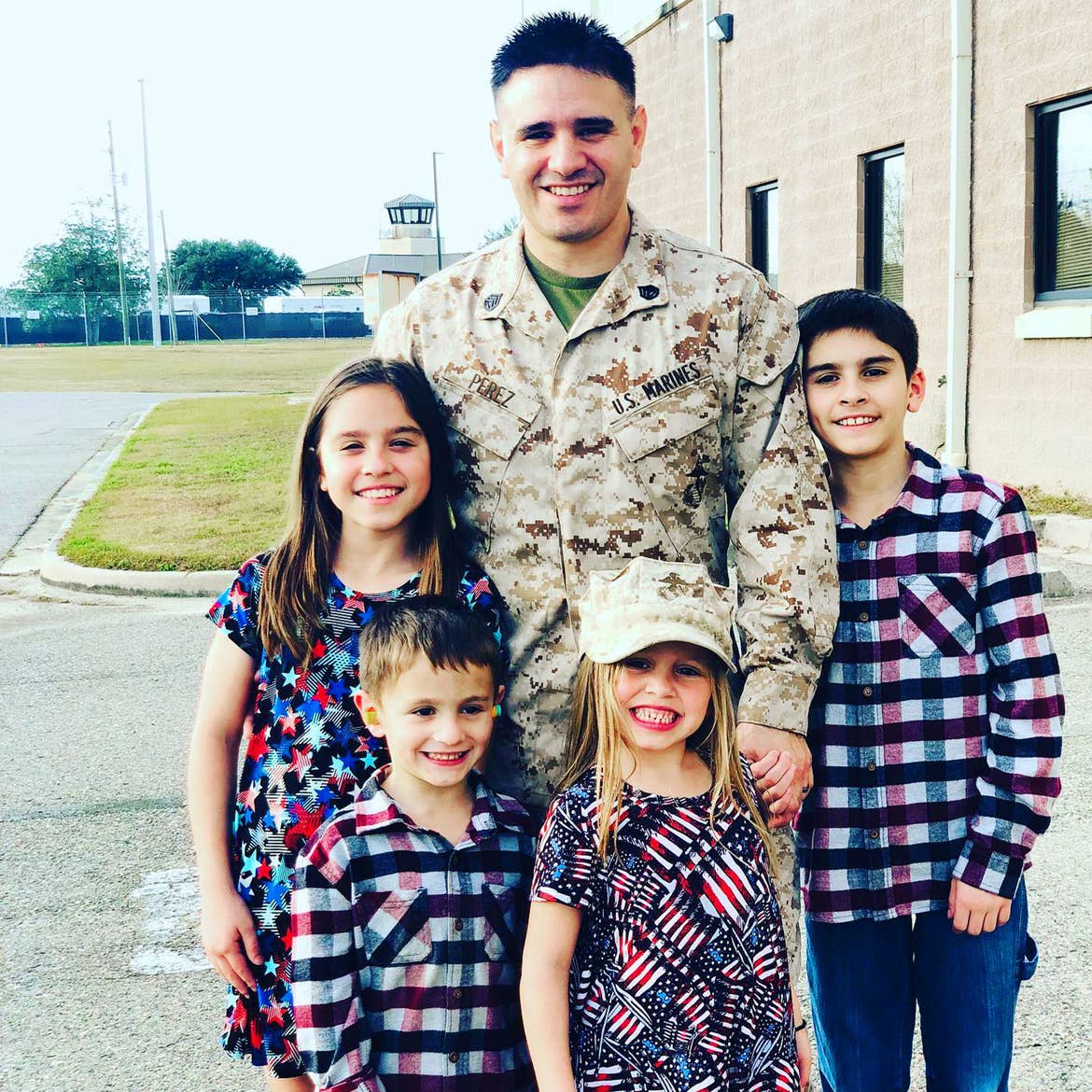 Featured Member, Sara Perezes children stand with their father, Sgt. Tommy Perez Jr. outdoors near a facility.