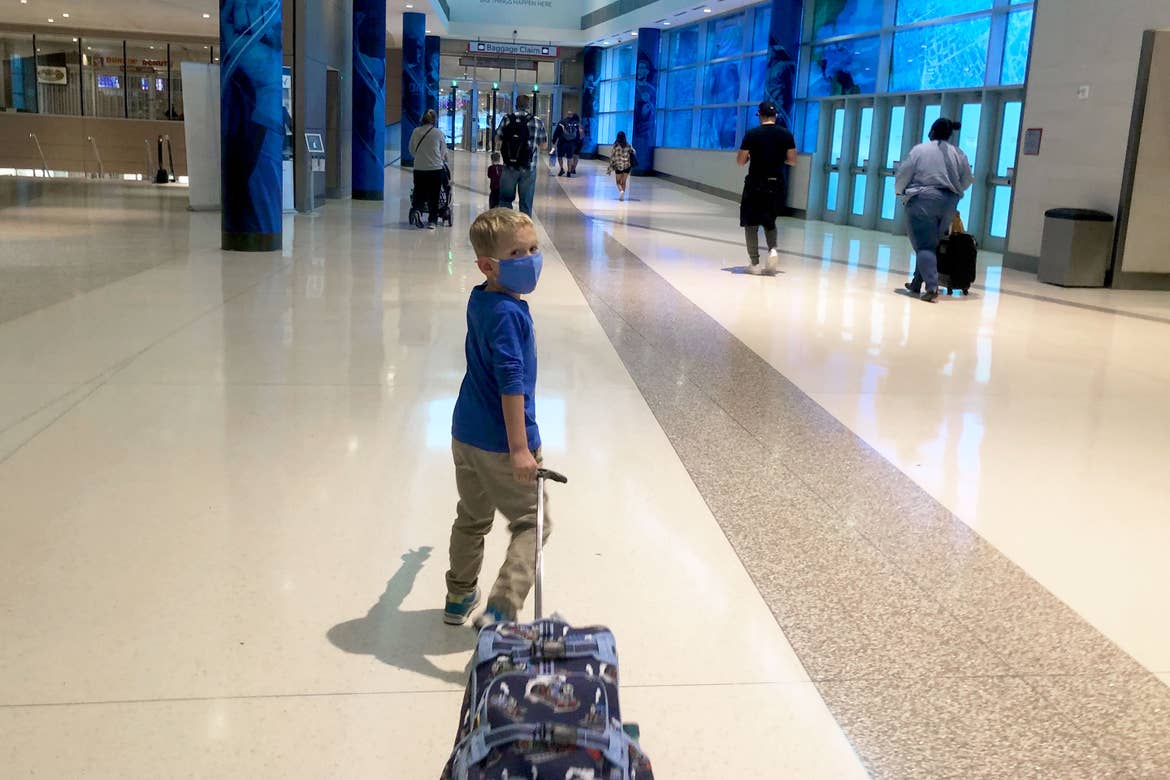 Sarah's son, Logan, pulls his suitcase wearing a mask they walk through the terminal.