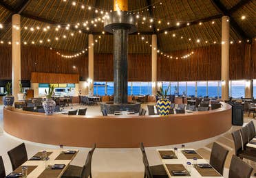 Oceanfront dining beneath a glowing palapa canopy.