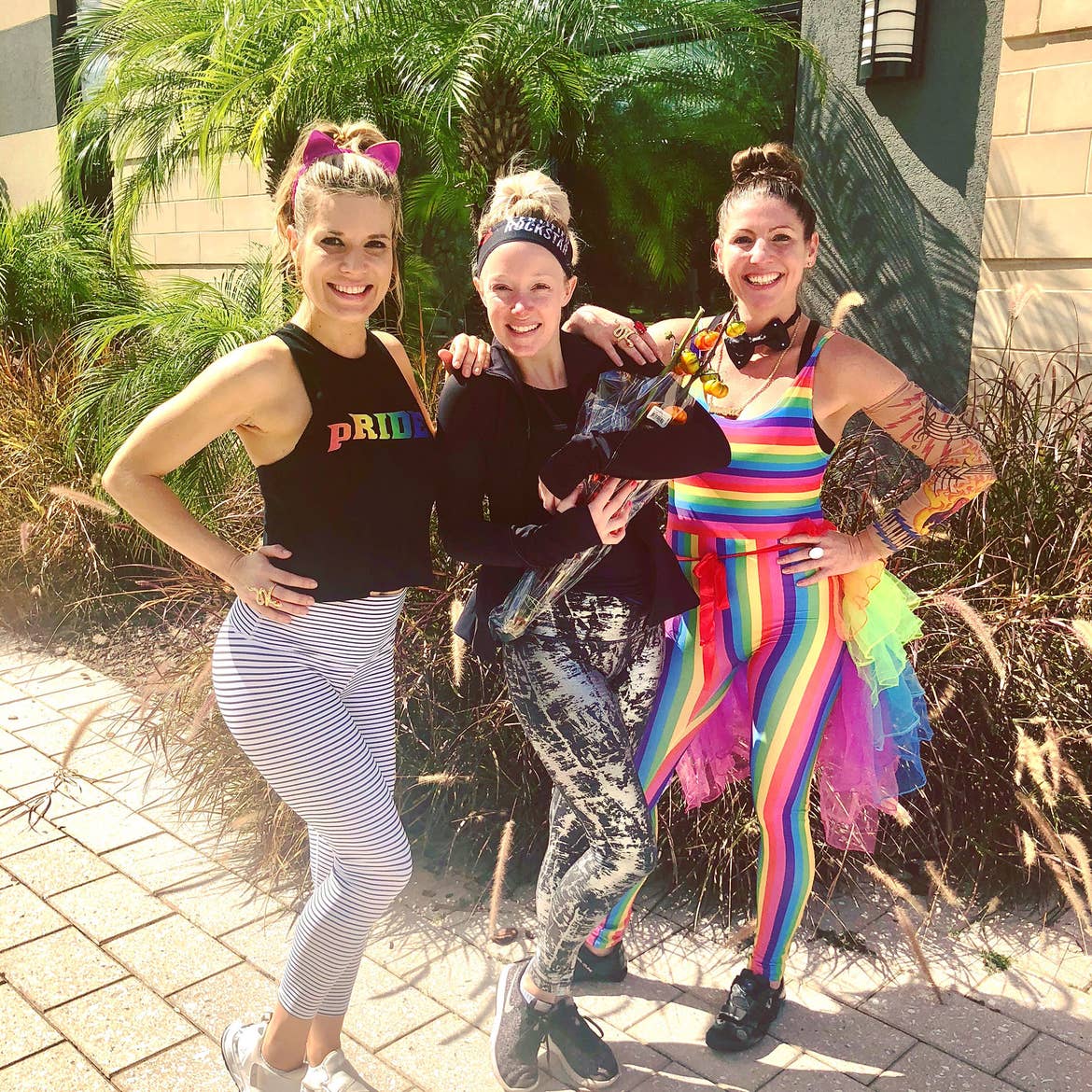 From left to right: Co-authors, Jessica, Molly and Christine wear PRIDE-inspired outfits together outdoors.
