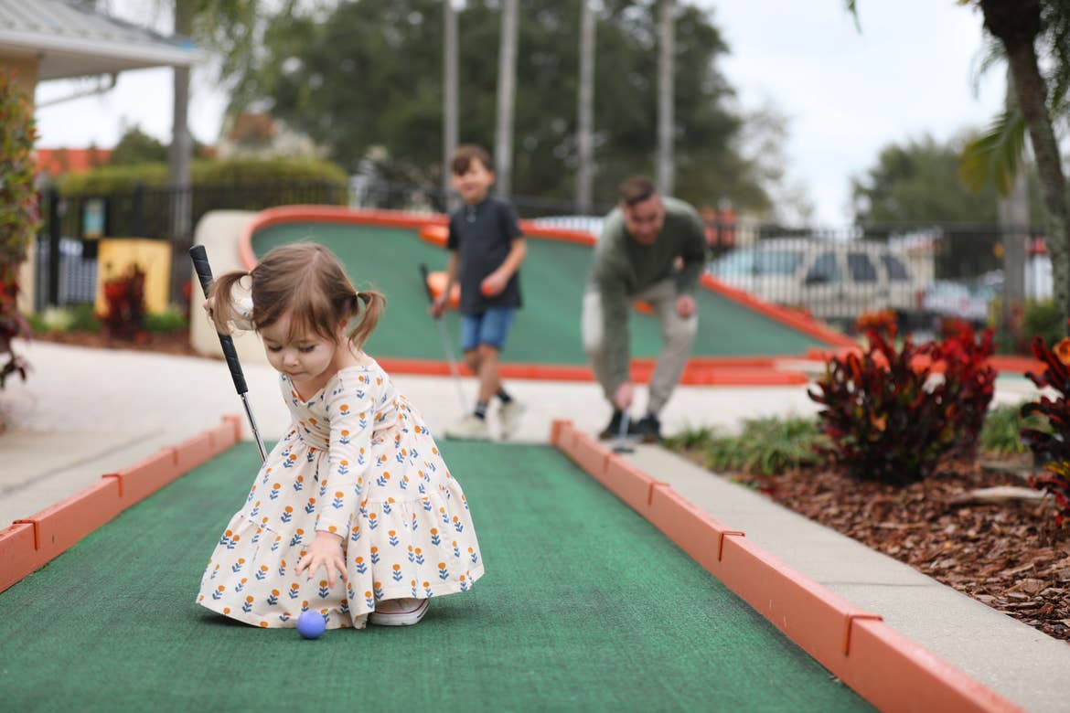 Mia St Clair's daughter picking up a blue golf ball at the mini golf course