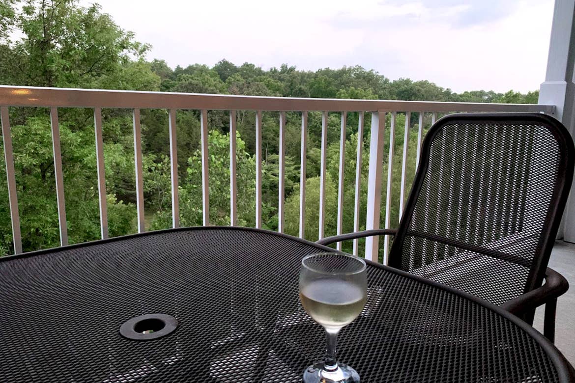 A glass of white wine placed on a patio table that overlooks lush trees.