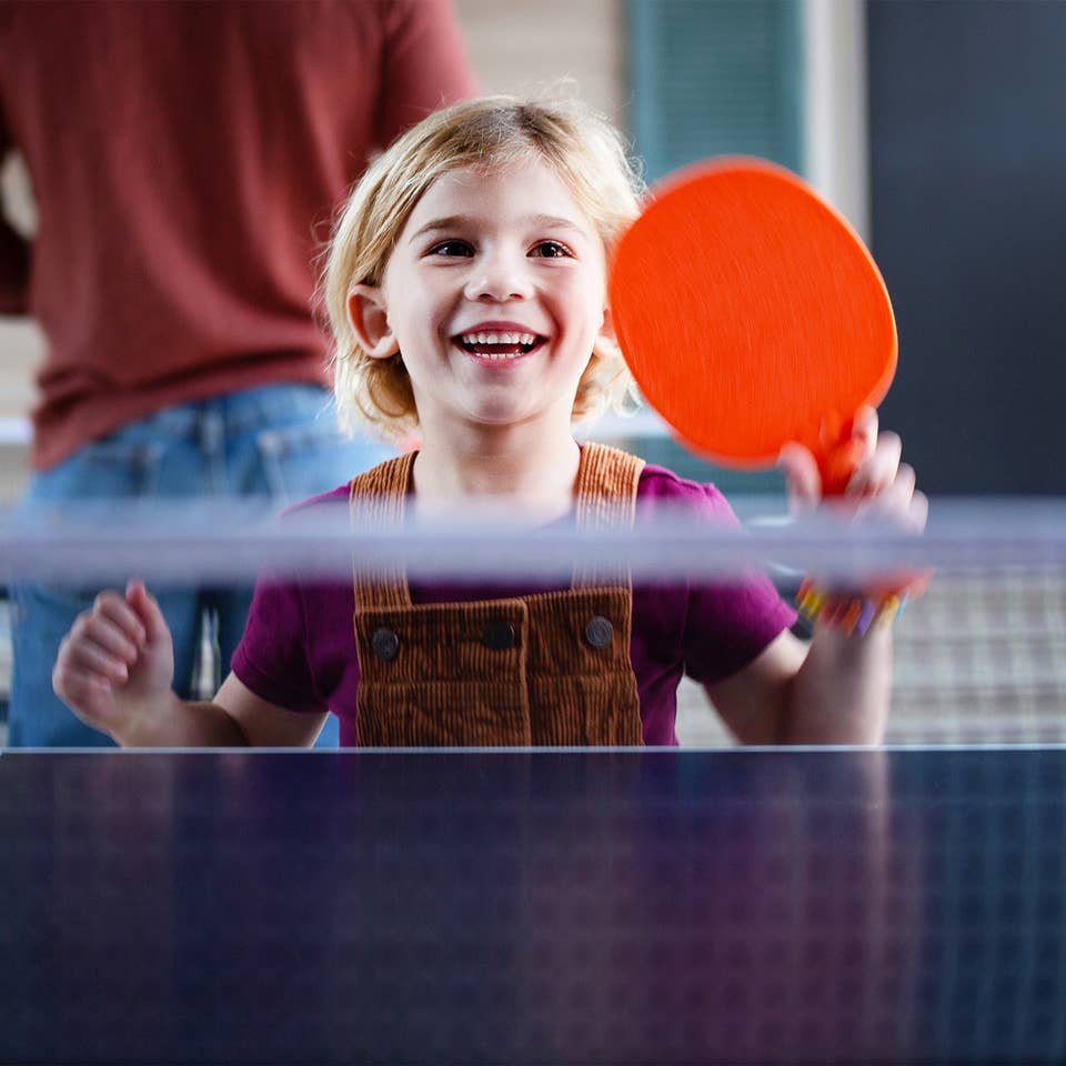 A young girl holding a paddle at a ping pong table