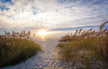 Cape Canaveral Beach sandy beach walkway with grass on the sides and a sunset overlooking the water in the distance.