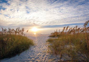 Cape Canaveral Beach sandy beach walkway with grass on the sides and a sunset overlooking the water in the distance.