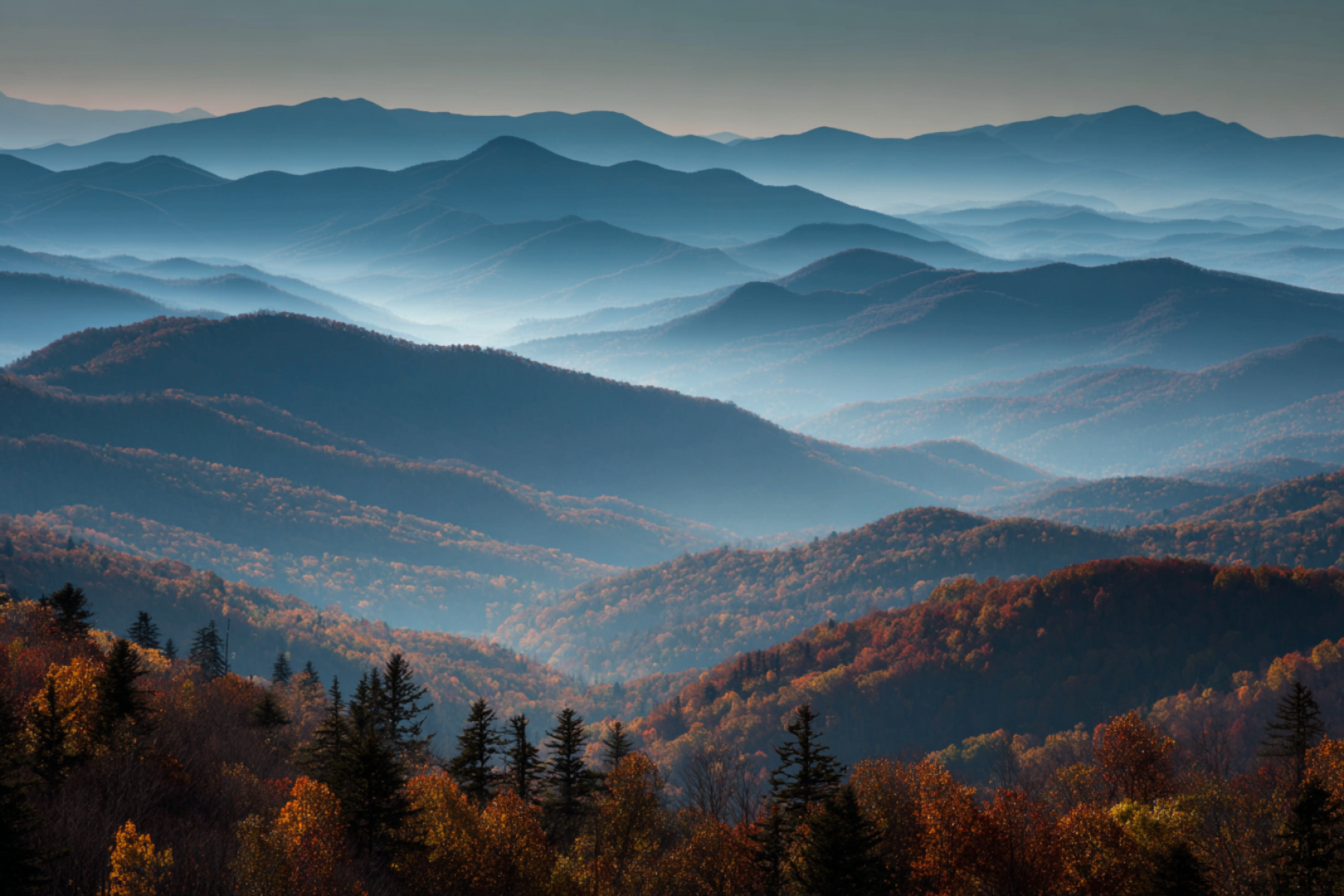 Layered Smoky Mountains with mist and autumn-colored forest in foreground.