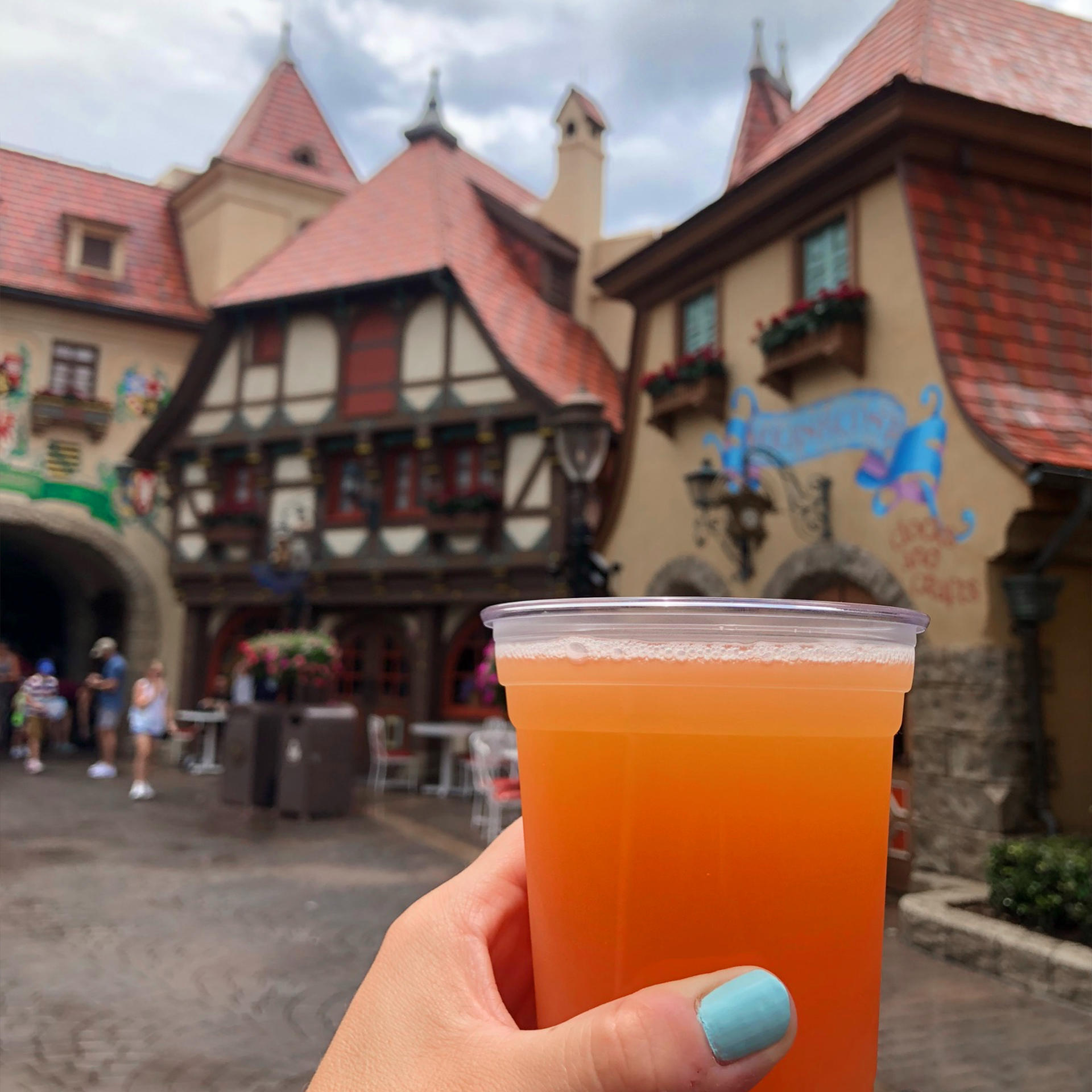 A hand holds a plastic cup of beer near the Germany Pavilion at Epcot in the rain.