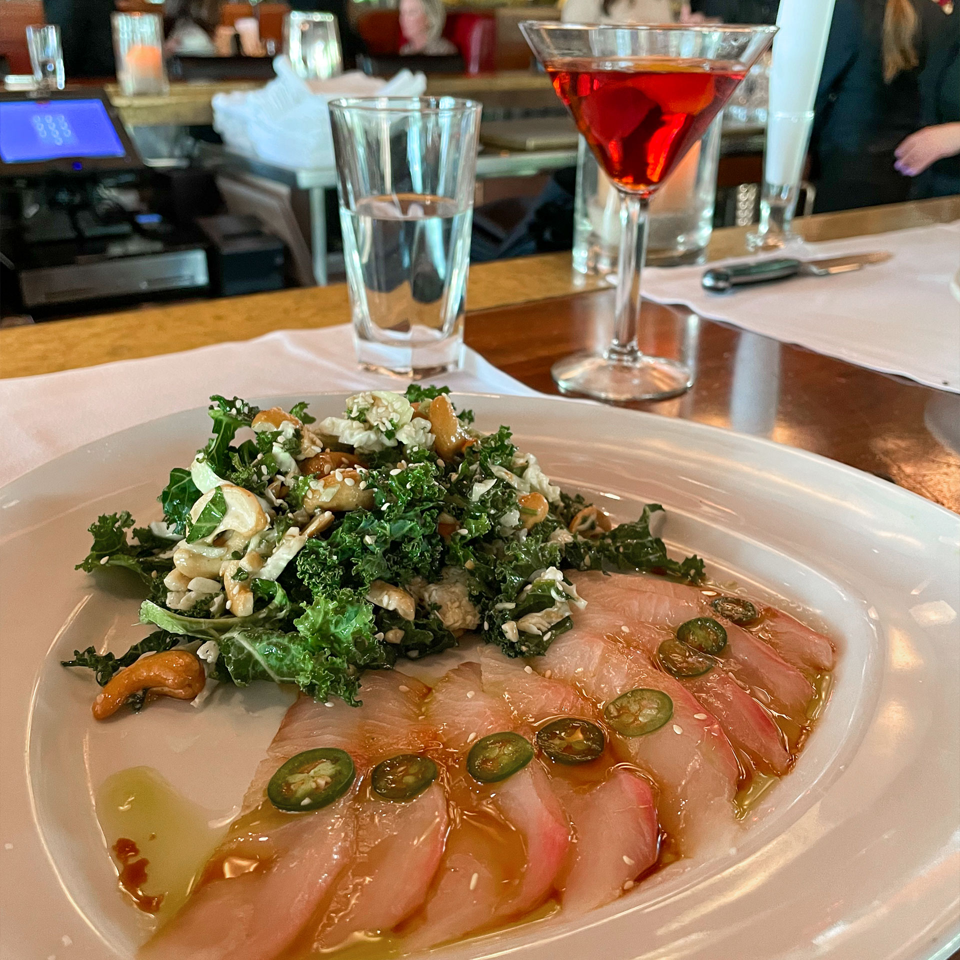 A dining plate with an entree is placed on a tabletop near a glass of water and martini glass.