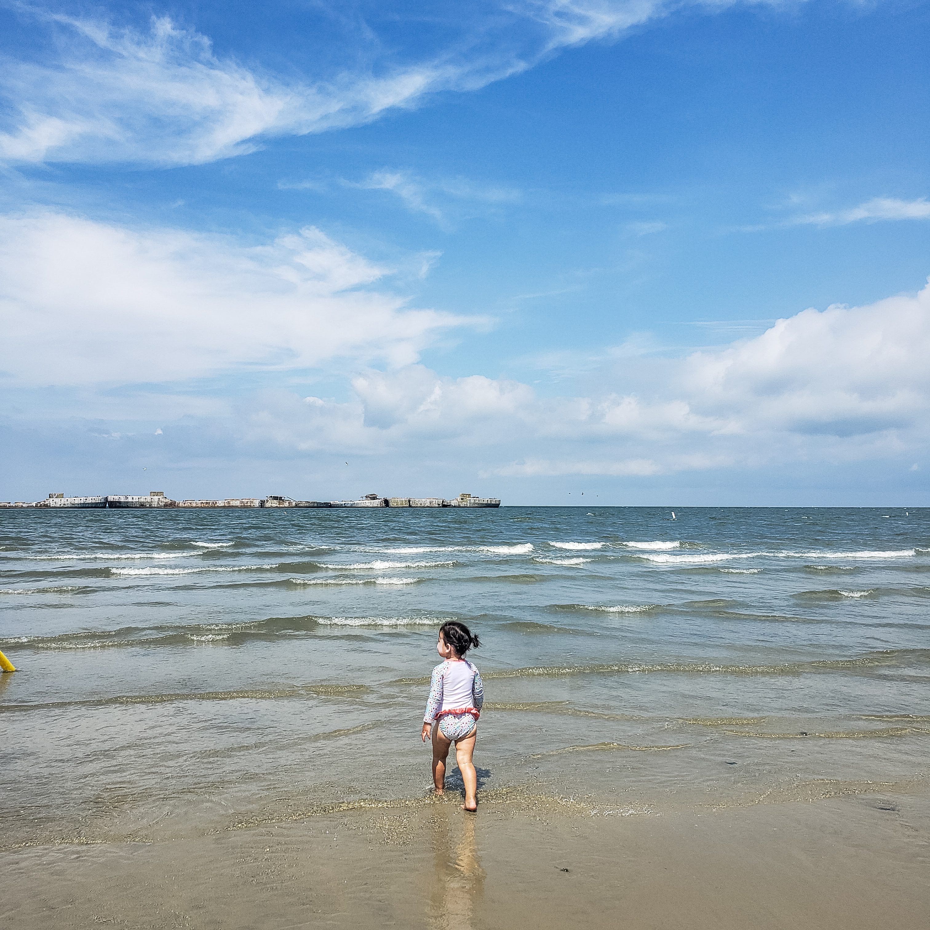 Angelica's daughter walking on the beach toward the waves, looking at the concrete fleet.