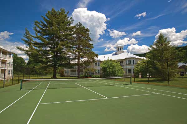 Tennis court surrounded by large trees at Oak n' Spruce Resort in South Lee, Massachusetts