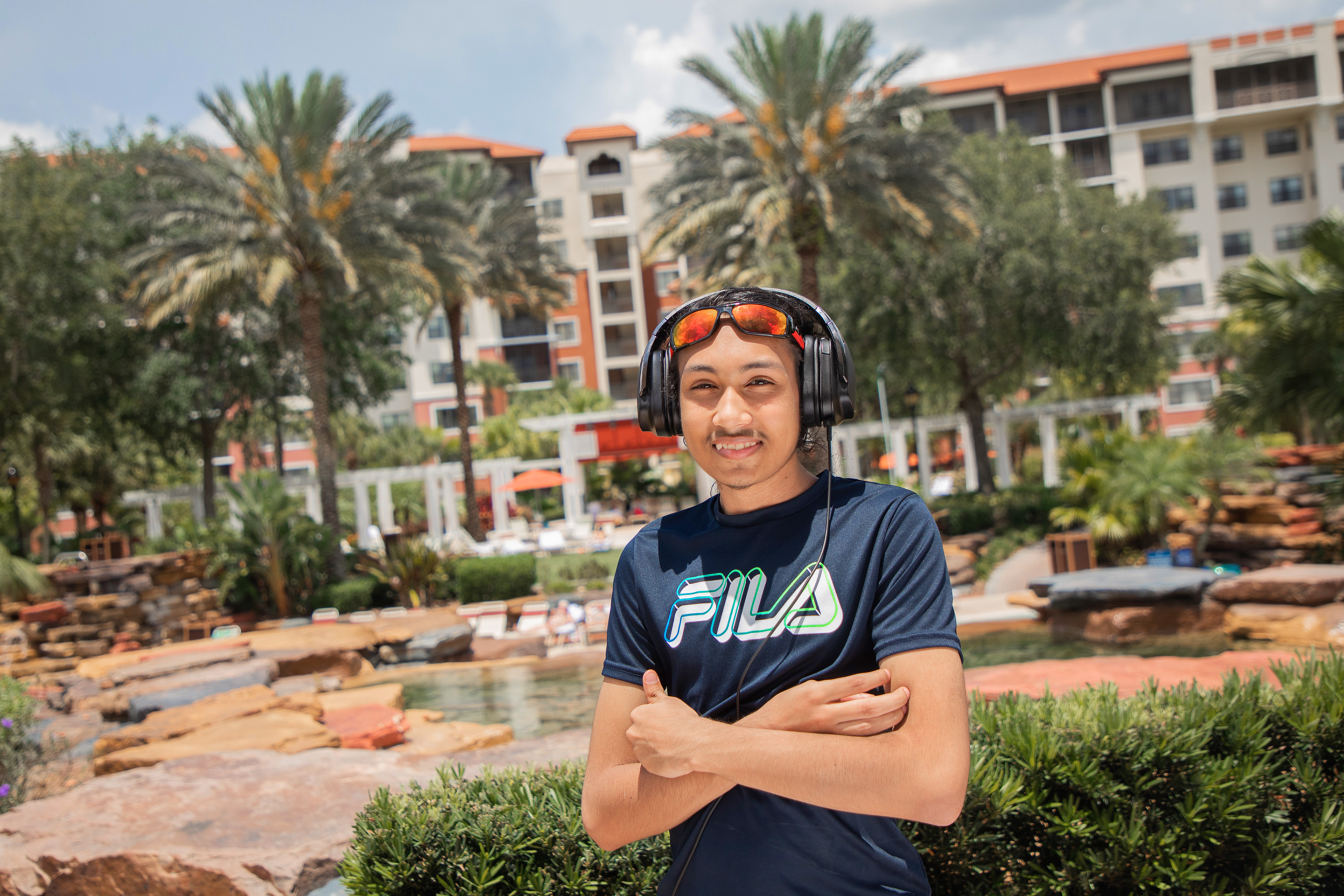 Special Olympic Athlete, Roan Luallen, smiles as he wears a black shirt and a headset in front of the lazy river at our Orange Lake Resort located in Orlando, Florida.