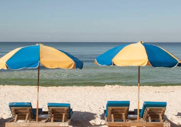 View of four beach chairs under two umbrellas at Panama City Beach in Florida.