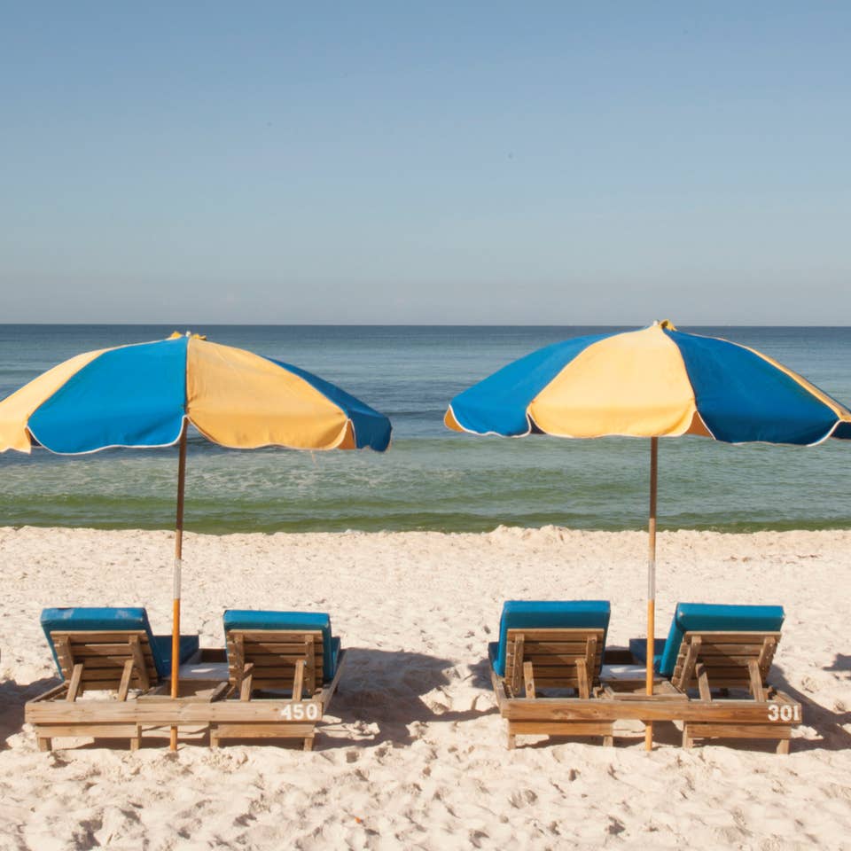 View of four beach chairs under two umbrellas at Panama City Beach in Florida.