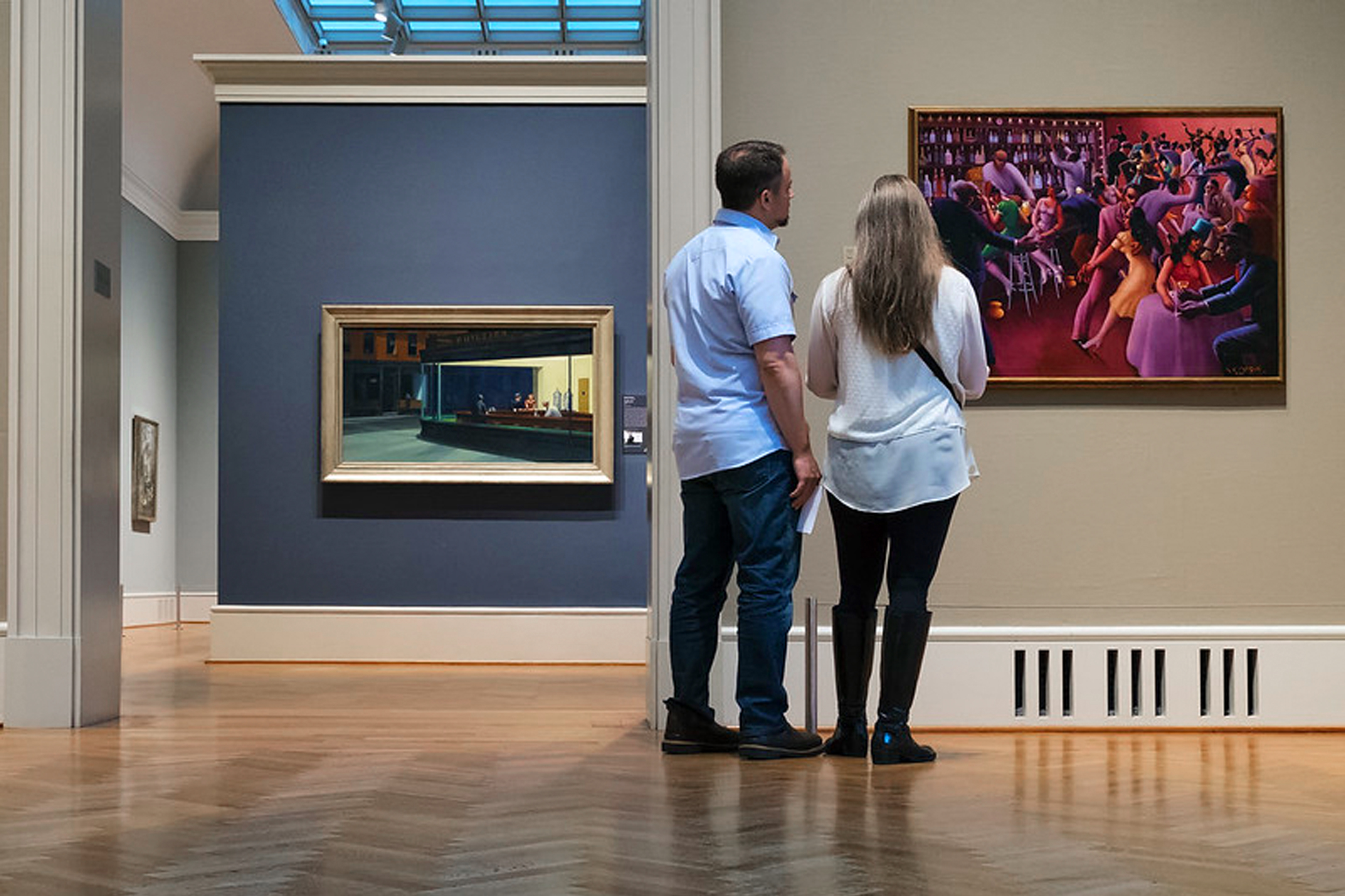 A man and woman observe a painting in a gallery.