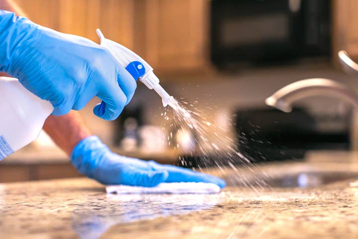 Hands wearing gloves and spraying cleaning solution on a kitchen counter