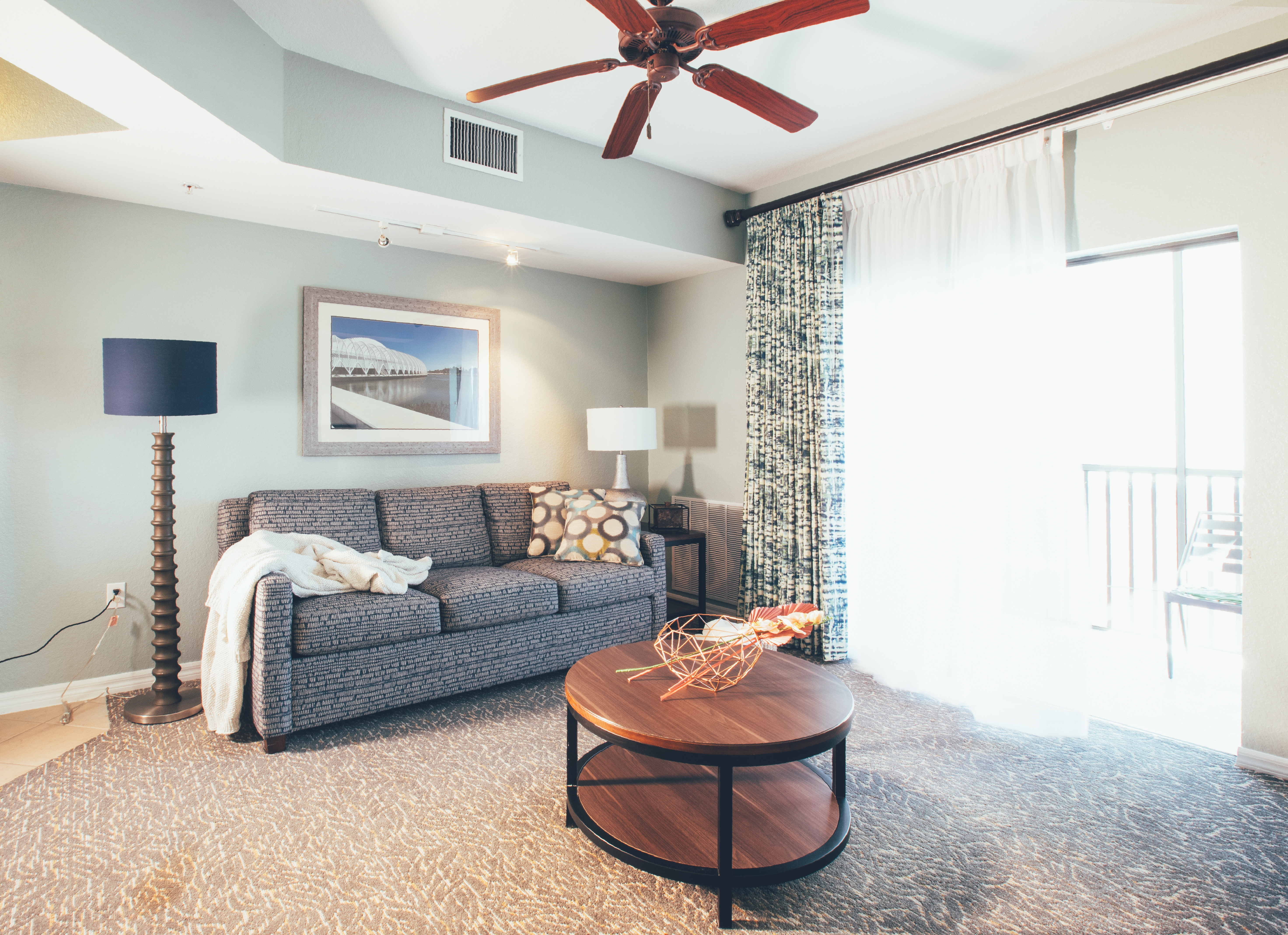 Living room with couch, access to balcony, and ceiling fan in a one bedroom villa in River Island at Orange Lake Resort near Orlando, Florida