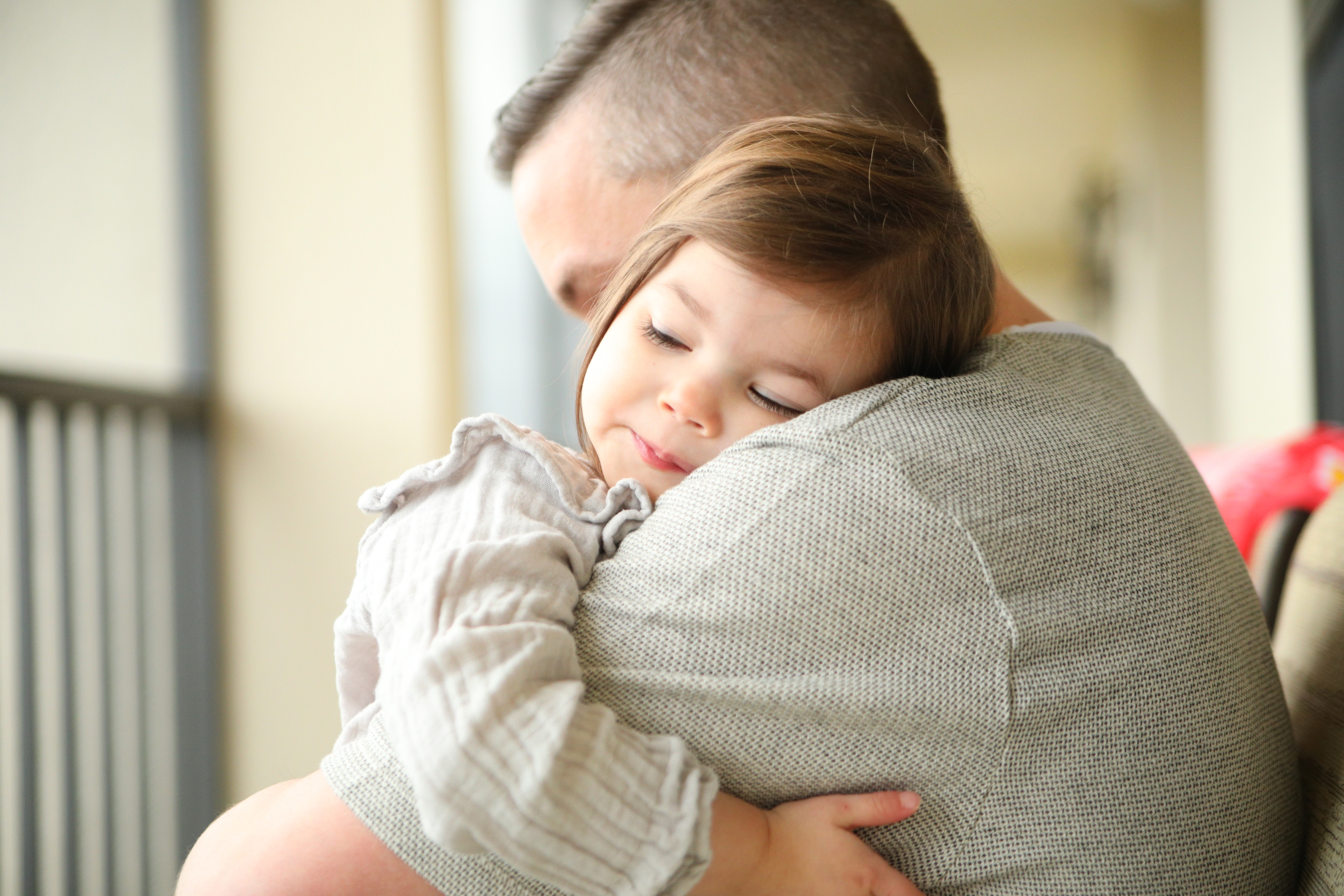 Little girl asleep on her father's shoulder as they sit on a screened-in patio.