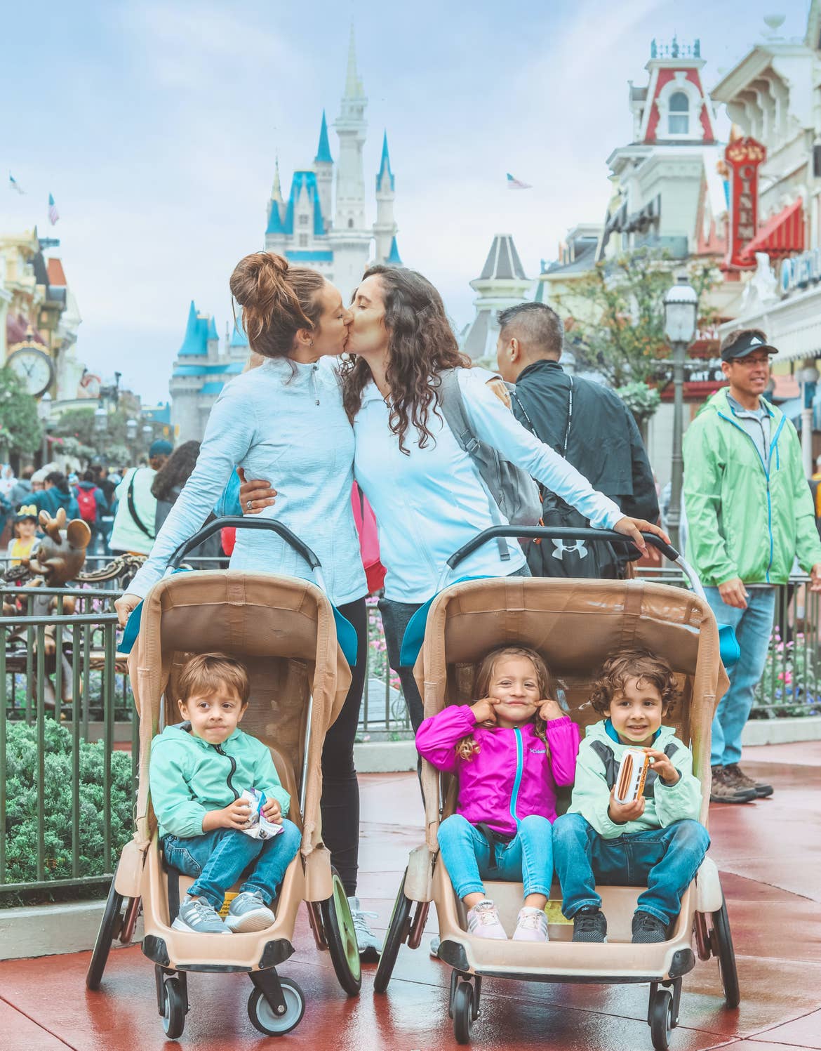 Raff and her wife with their three kids in strollers in front of them with the castle at Magic Kingdom Theme Park in Walt Disney World Resort in the background.